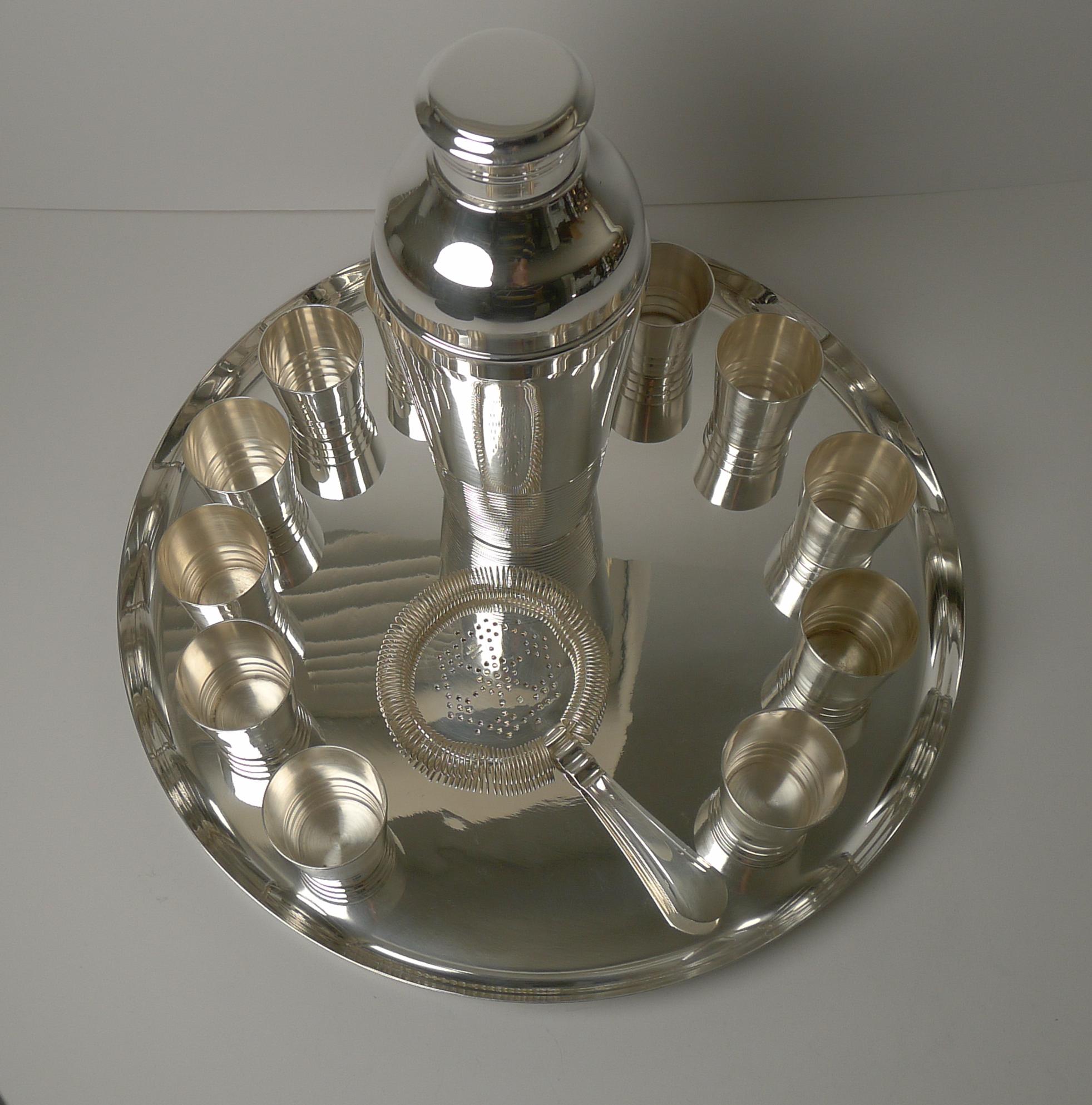 A real find, a wonderful silver plated cocktail set comprising a large circular tray, twelve small shot glasses / cups, a strainer and large cocktail shaker.

The design of the shaker and cups is 