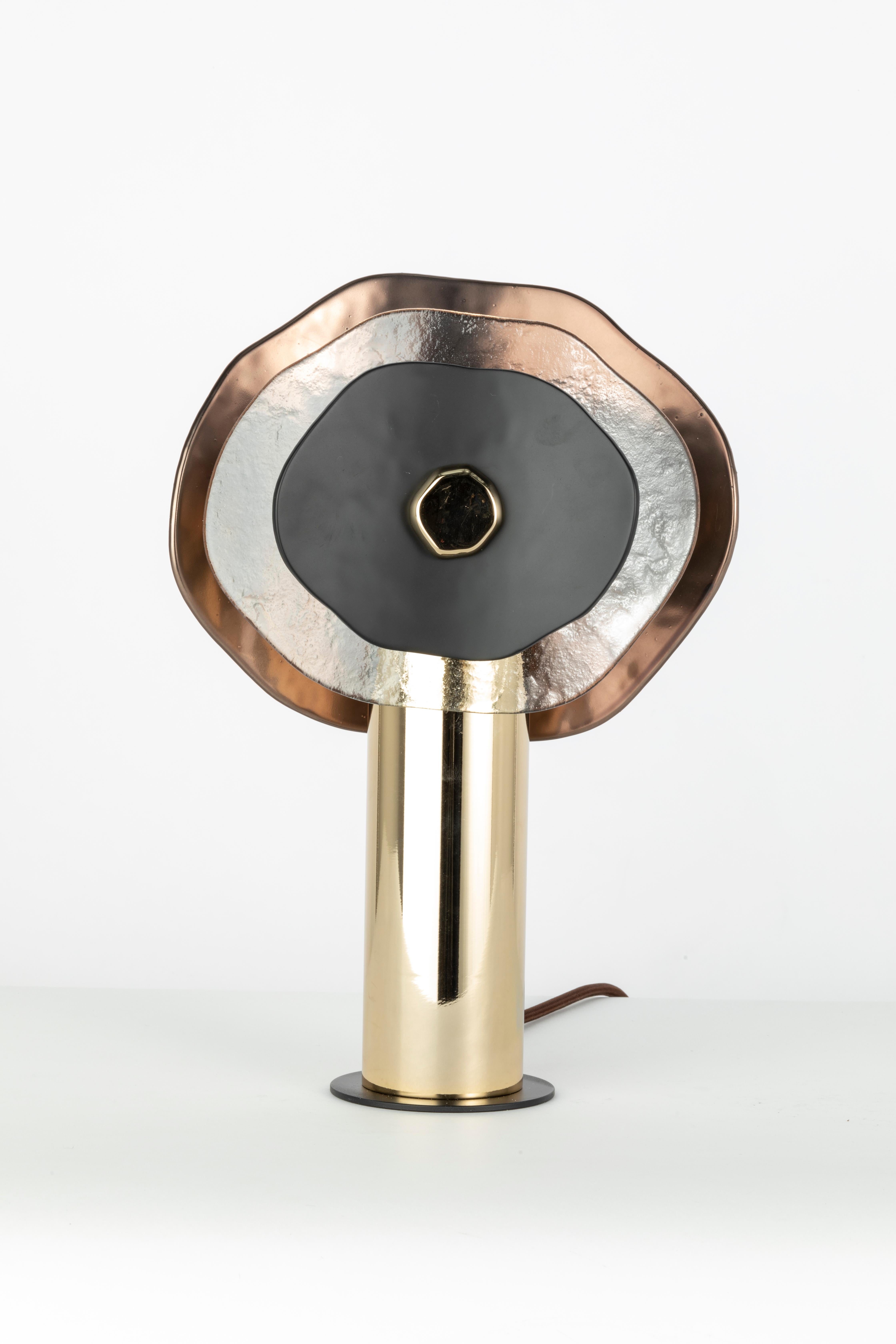 Lampada da tavolo media altezza. Composizione di petali in vetro trasparente, finitura bronzo semilucido e nero matte. Minuteria metallica in oro chiaro lucido; cavo di seta marrone. Una luce centrale; diffusore in vetro satinato e copertura in