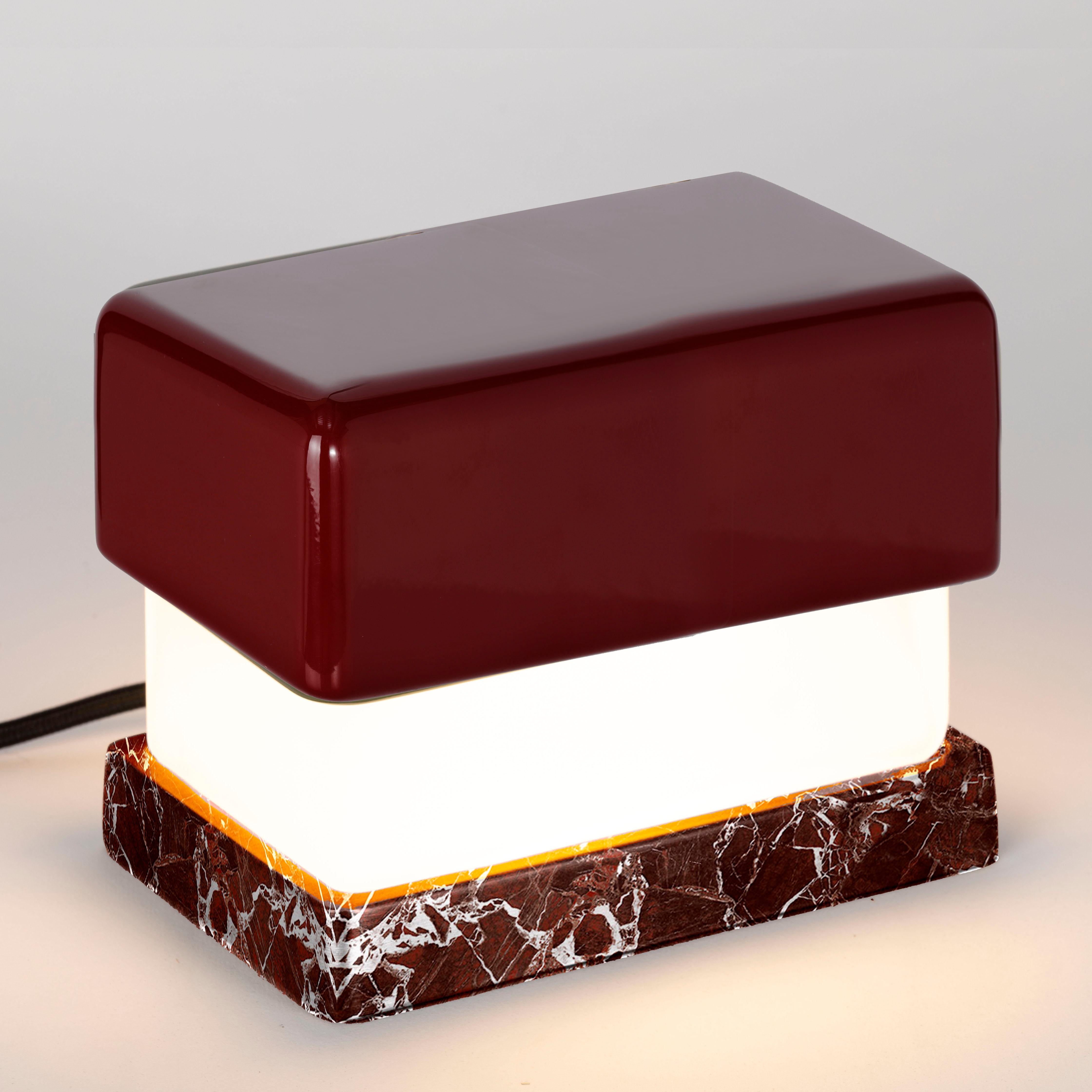 Pequeña lámpara de mesa. Tapa superior de madera lacada brillante de color burdeos; difusor de cristal esmerilado. Base de mármol Levanto. Cable negro satinado.
Diseñado por Matteo Bianchi para Officina Luce.

1 módulo LED con transformador, todo