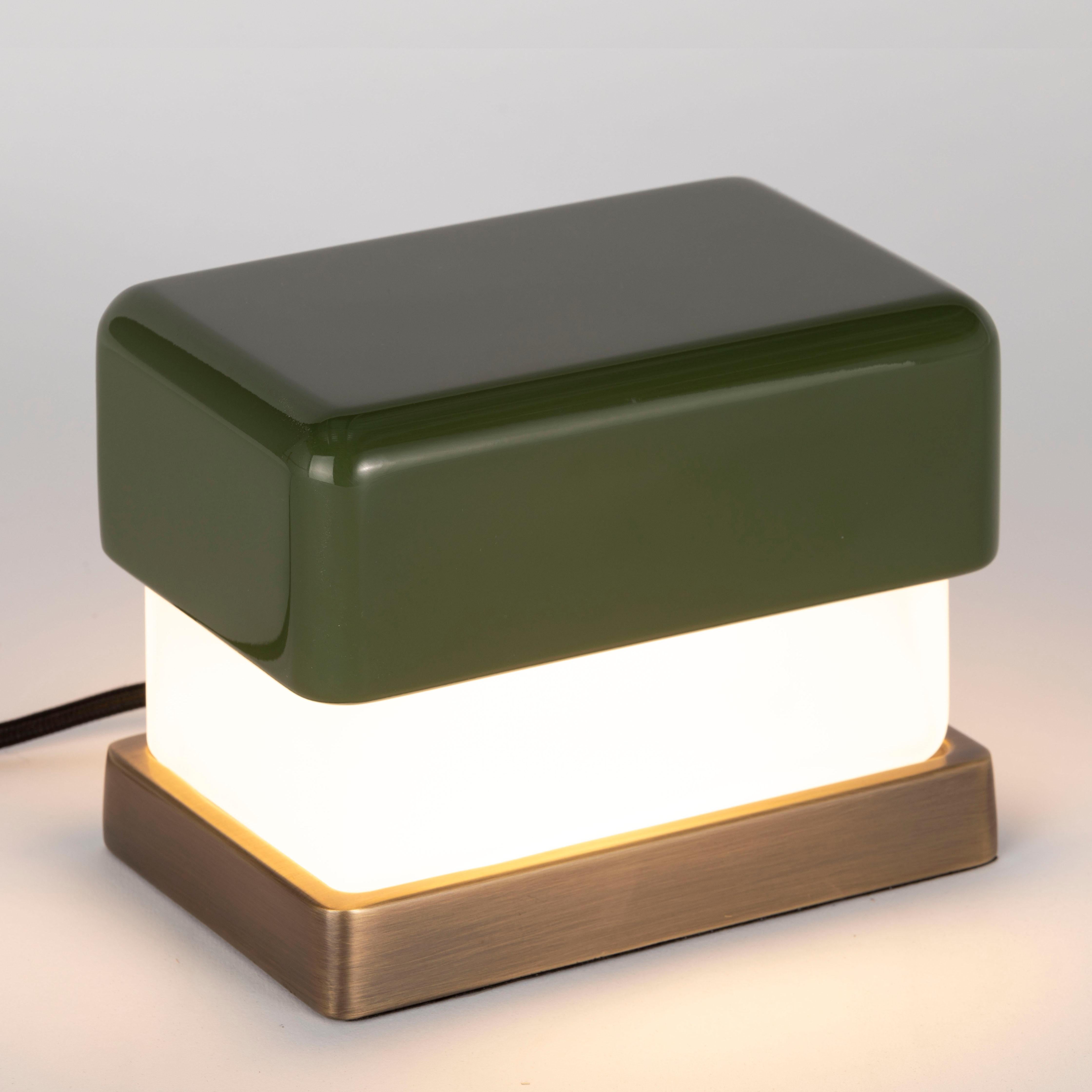 Lampada da tavolo piccola. Calotta superiore in legno laccato verde lucido; vetro diffusore satinato. Base in ottone pieno. Cavo satinato nero.
Disegnato da Matteo Bianchi per Officina Luce.

1 x modulo LED con trasformatore, tutto incluso. 
