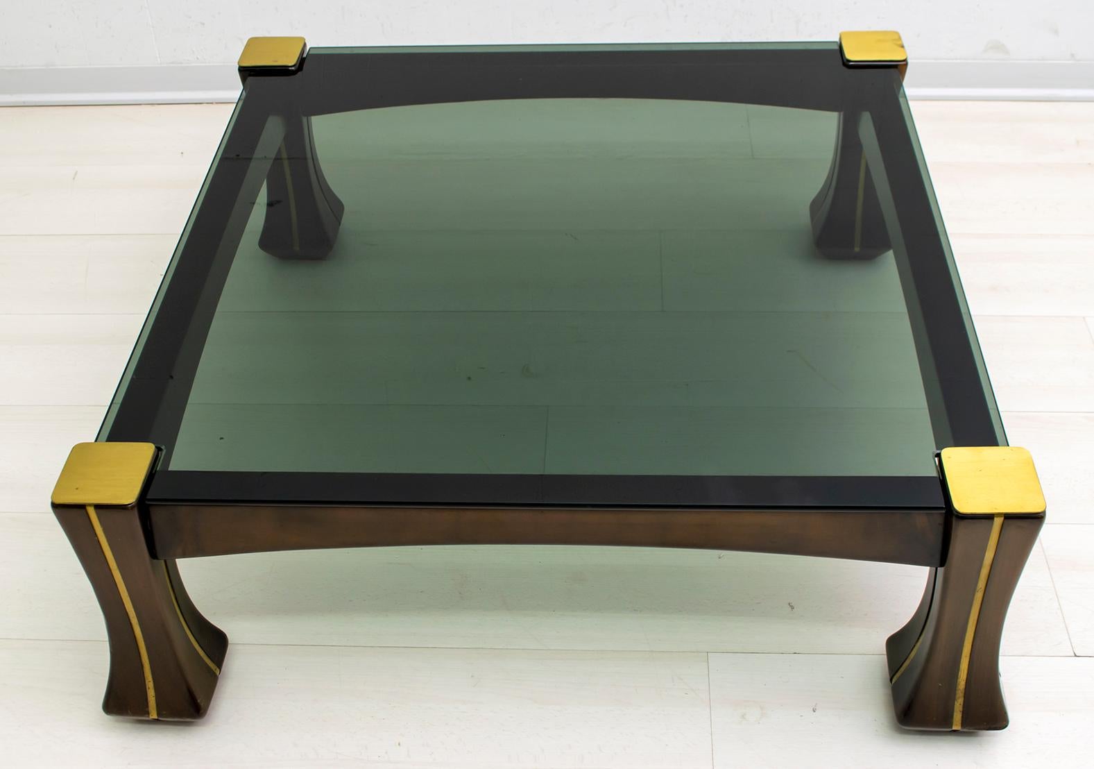 This coffee table was designed by Luciano Frigerio. It is in wood with brass friezes, the top is in smoked glass. This model is part of the 