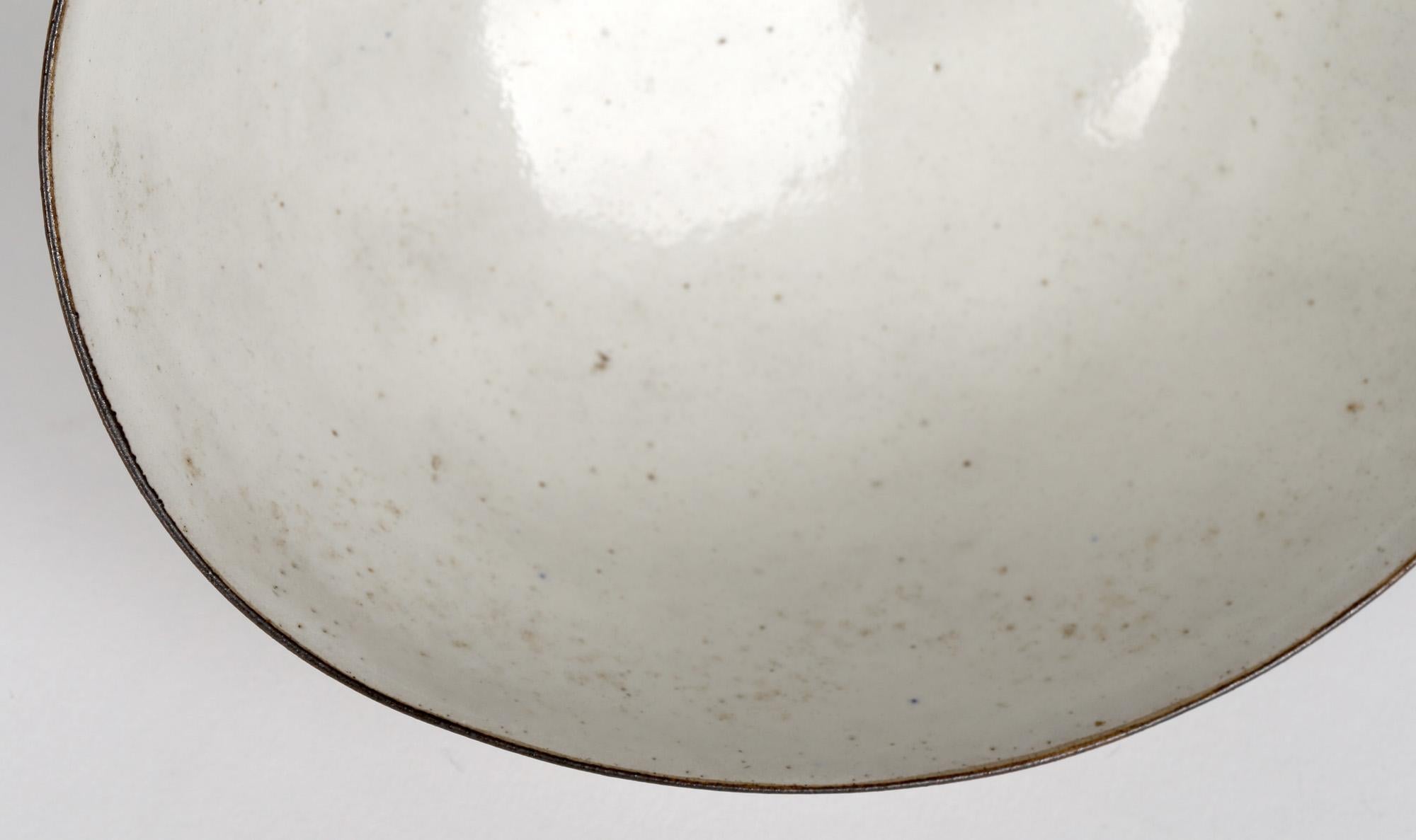 Stoneware oatmeal glazed bowl with small crater and speckled inclusions with a wavy rim with a fine manganese glazed edge by Lucie Rie (Austrian/British, 1902-1995) dating from around 1965. Impressed LR seal mark to the base.

In good condition.
 