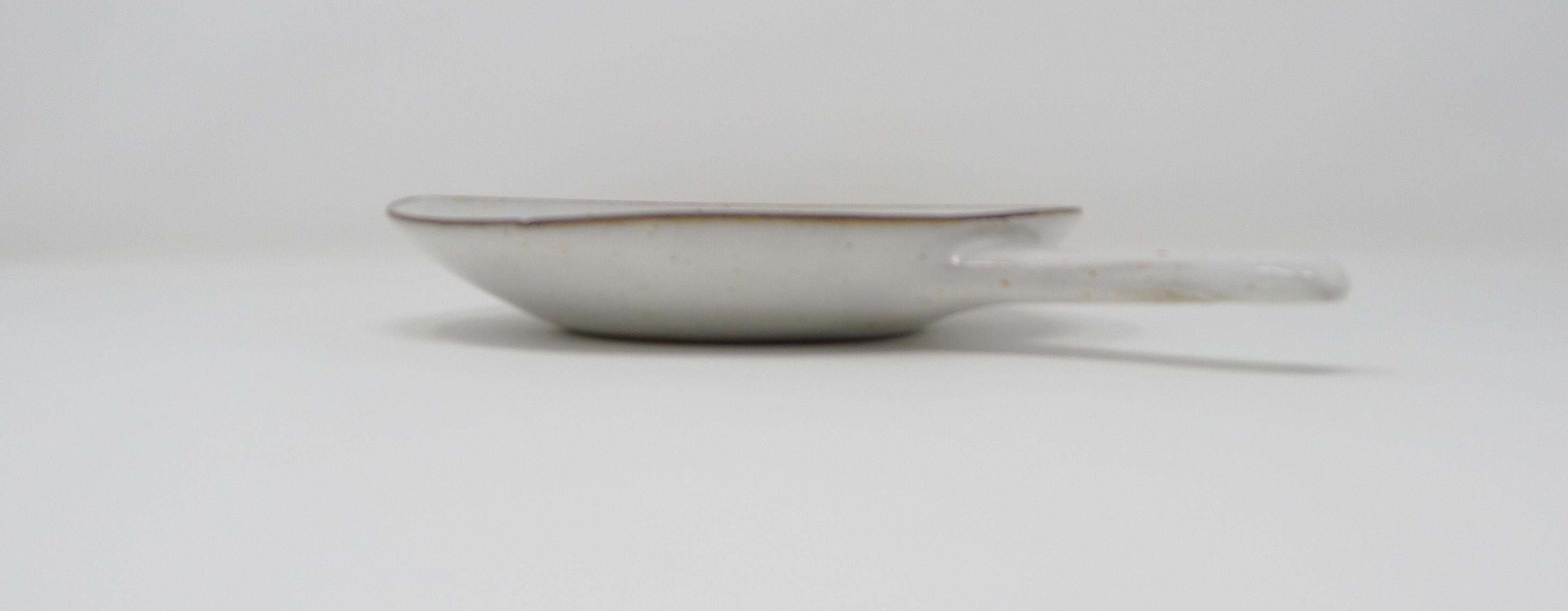 Lucie Rie; Elegant handled shallow stoneware dish in cream with manganese oxide lip, late 1950s.
Underside signed with impressed artists seal.
