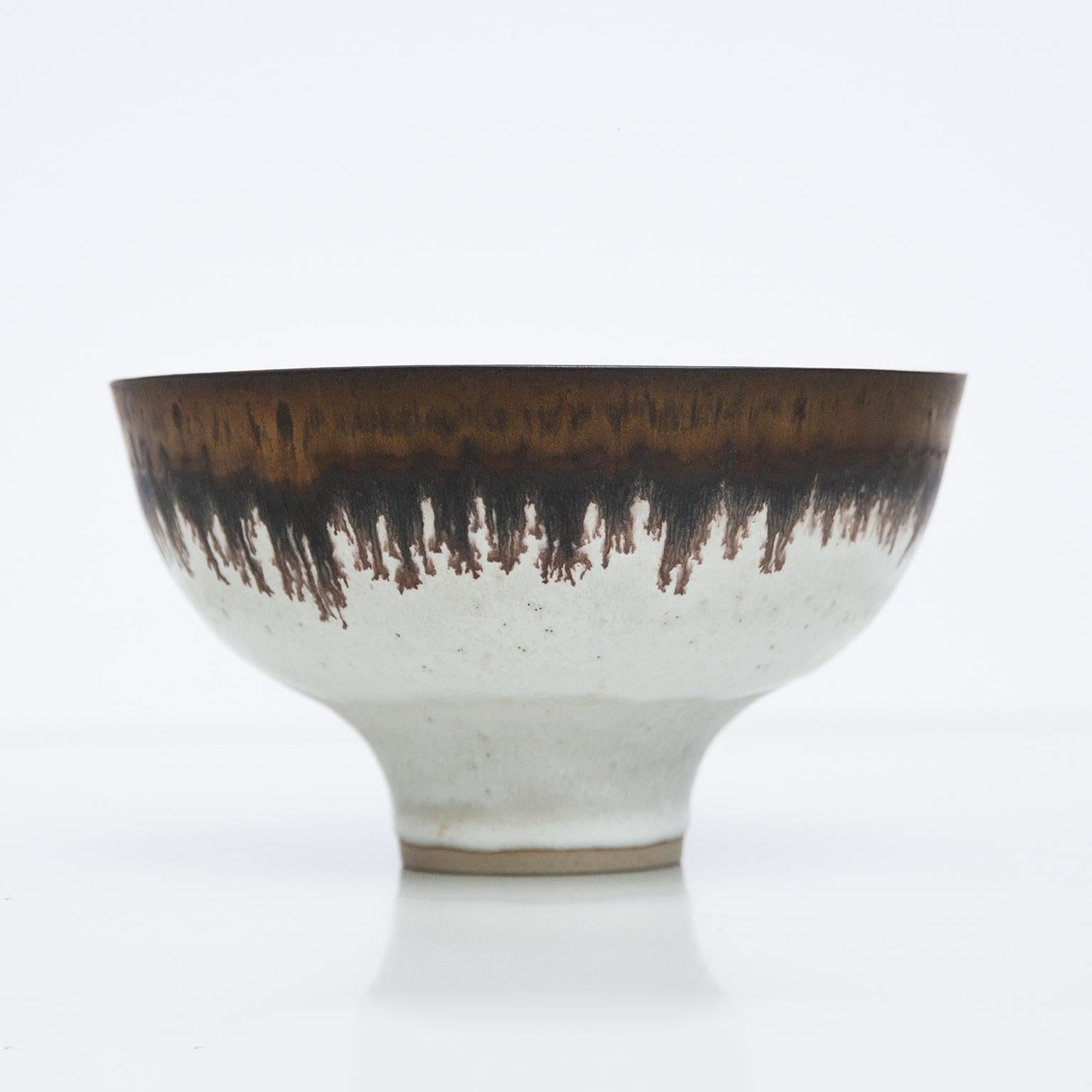 Bowl with manganese rim. Circa 1980. Porcelain. White, partially stone-grey and sand-colored grading and speckled glaze. The rim of the mouth inside and outside with a wide, bronze-coloured, shimmering manganese glaze band, ending in fine drops
