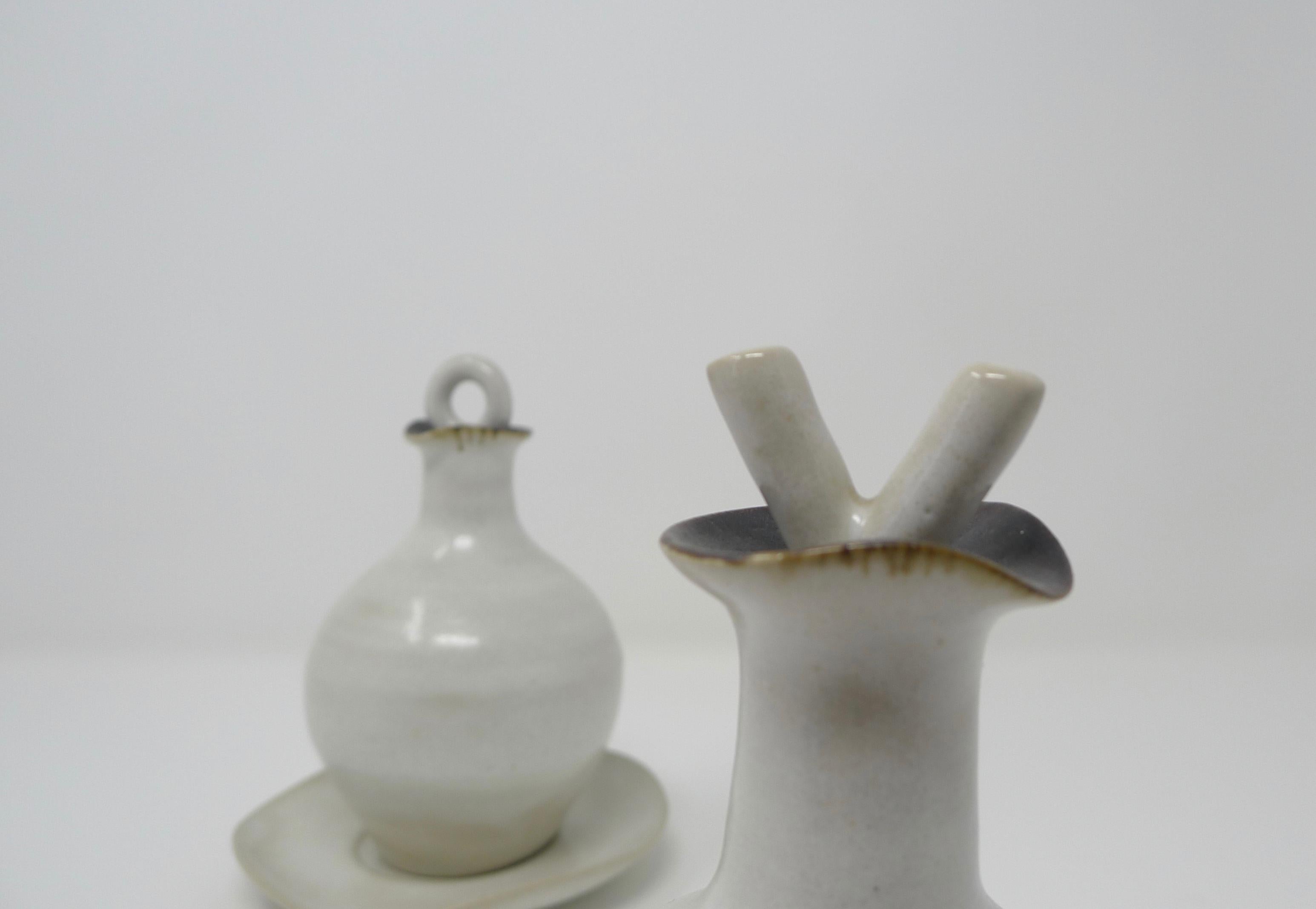 Lucie Rie; Stoneware oil and vinegar set of textured white glaze and manganese rims. Stoppers are formed in the shape of an 