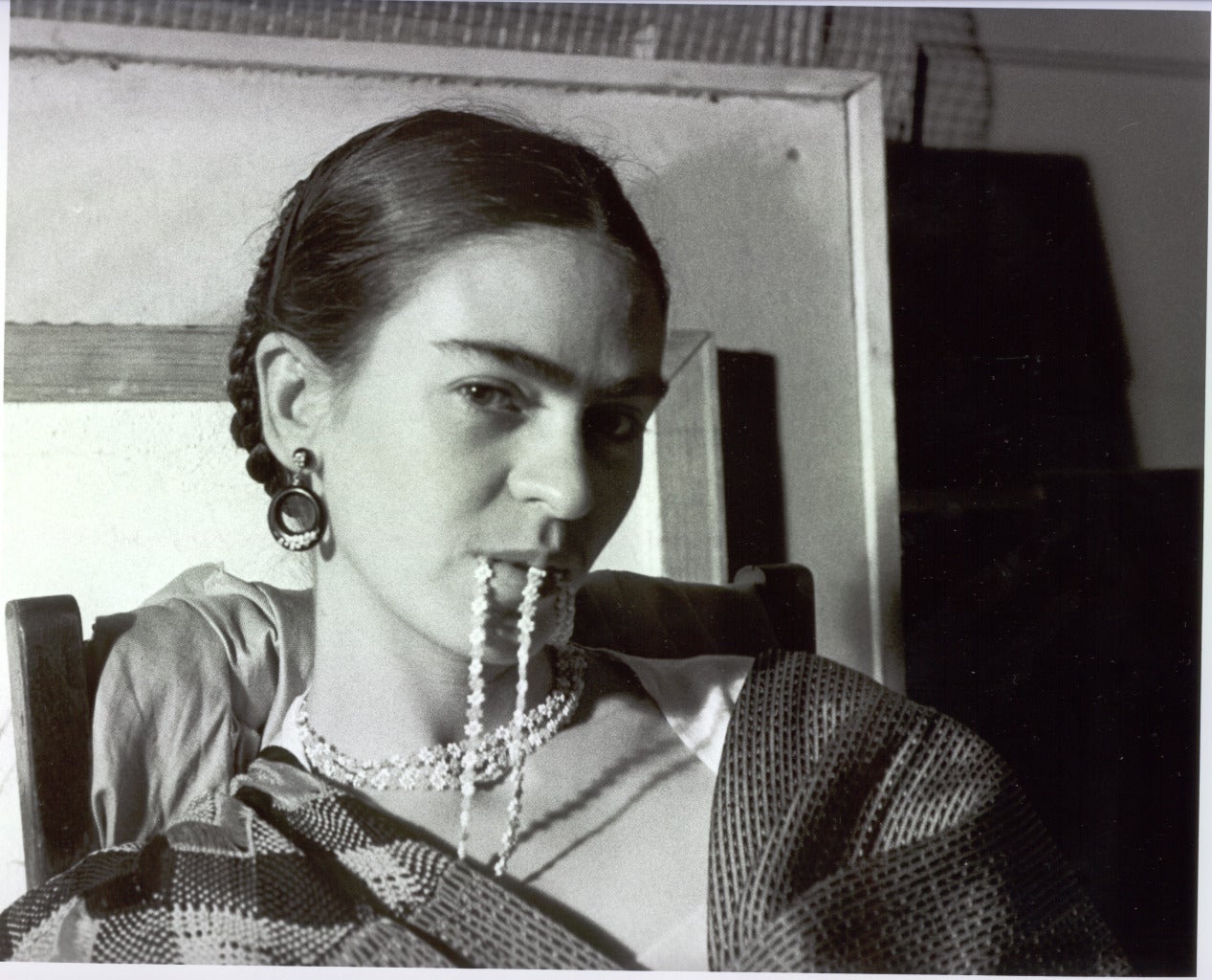 Frida Biting Her Necklace zeigt ein Porträt von Frida Kahlo, die auf einem Stuhl sitzt und in ihre Halskette beißt. Ihr Kopf ist leicht gedreht, während sie den Betrachter anschaut.

Frida Biting Her Necklace von Lucienne Bloch ist ein 8 1/4 x 10