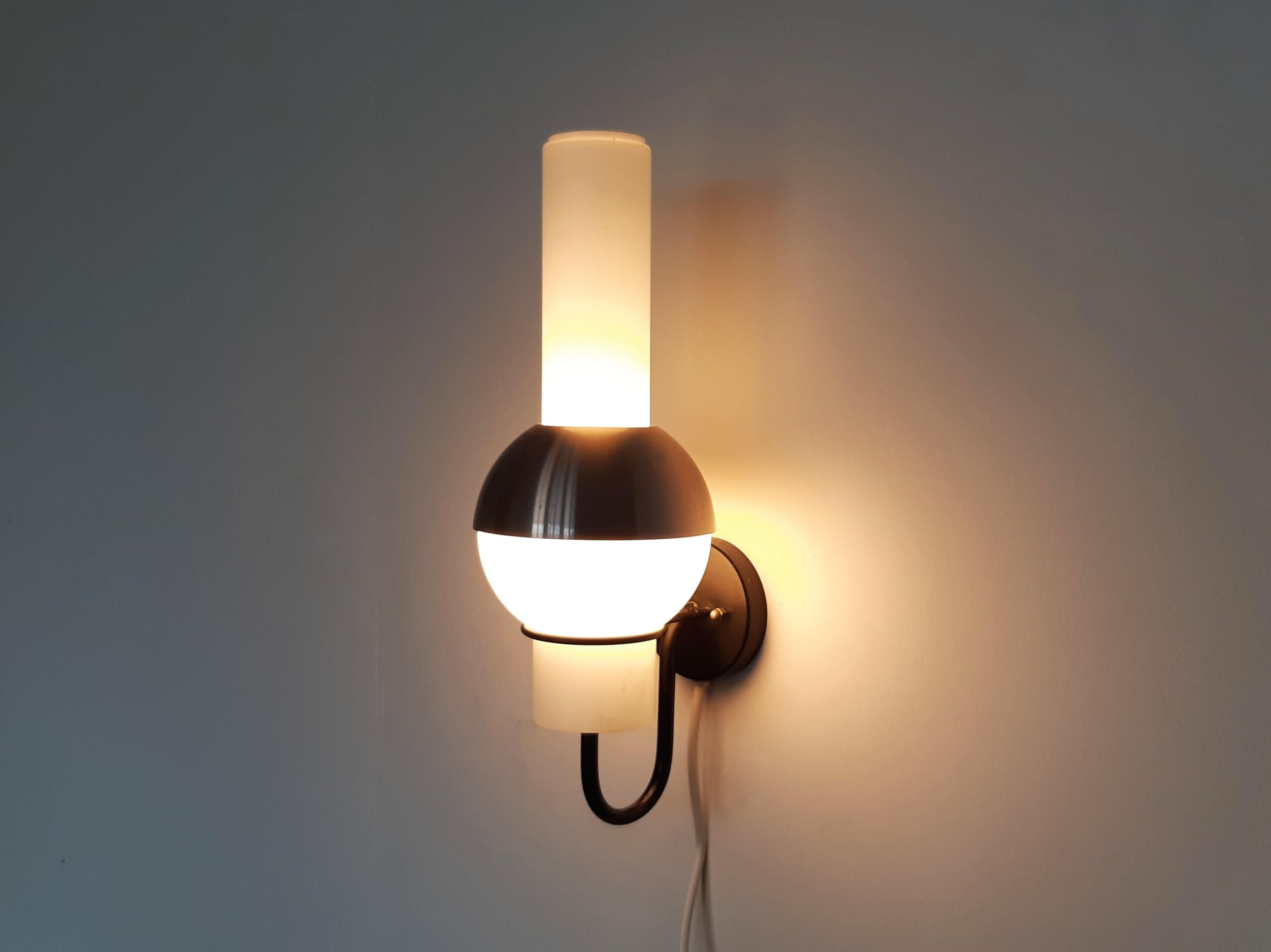 This wall lamp, model 'Lucifero' or 'Quinquet', was designed for RAAK in the 1960's. It has a black coated metal fixture with a ring that holds the opaline glass shade/diffuser. Decorated by a copper colored aluminum cap that can be removed. A