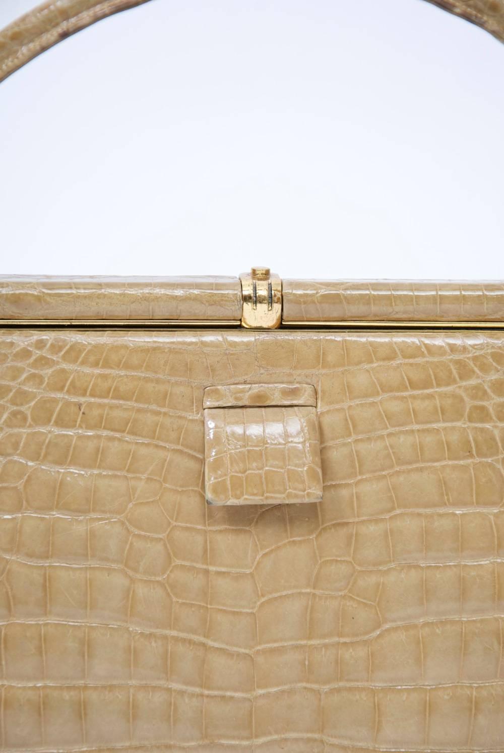 Classic 1960s Lucille de Paris handbag in neutral tan crocodile featuring a single handle and minimal goldtone clasp with small tab in front to help open. Camel leather interior with multiple side pockets, including one with snapped flap.
