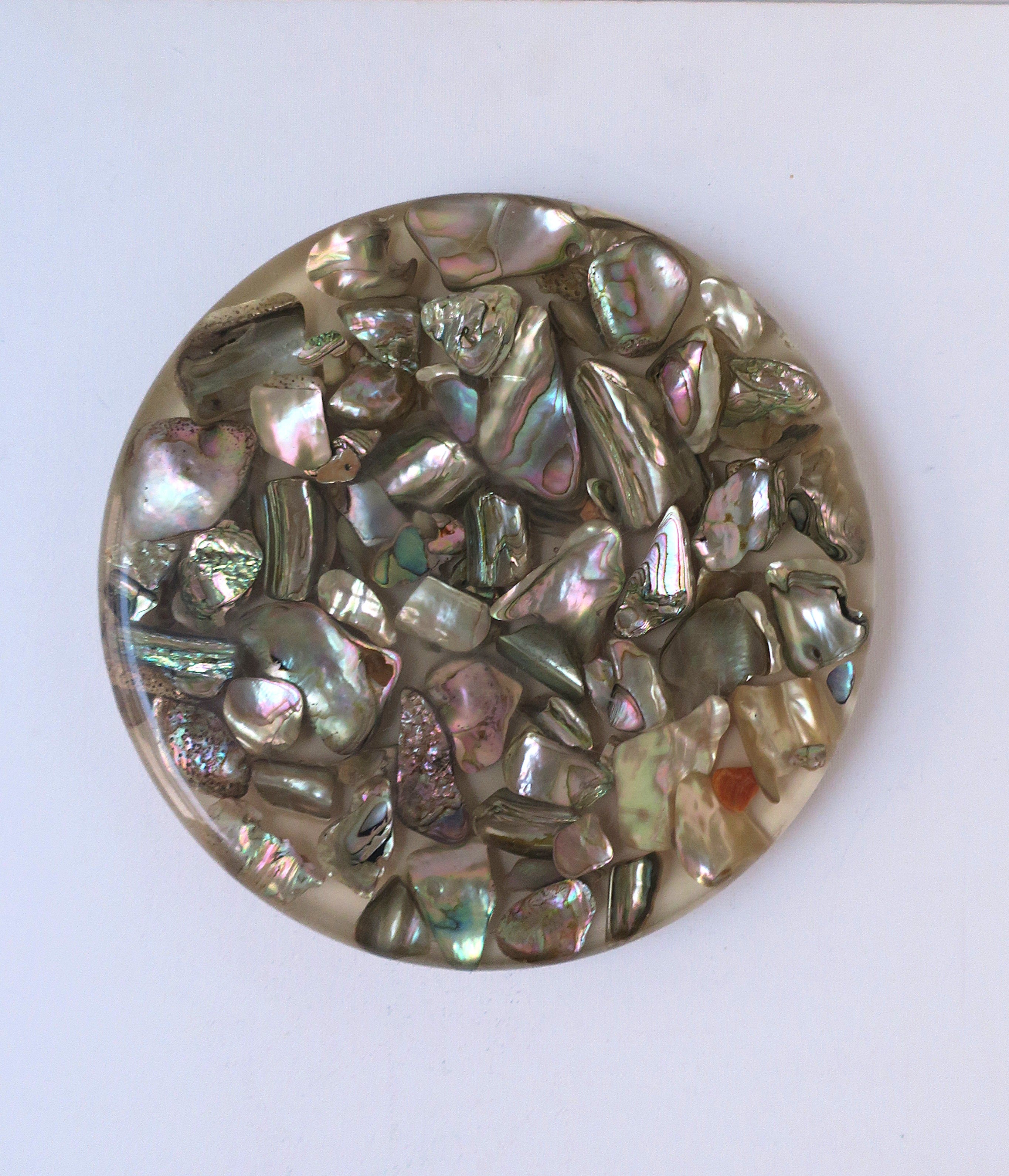 A Lucite acrylic and abalone seashell trivet, circa mid-20th century, 1960s, USA. Trivet is round with Lucite/acrylic encase abalone seashells, finished with three small feet on bottom. The abalone seashells, with beautiful iridescence, are from the