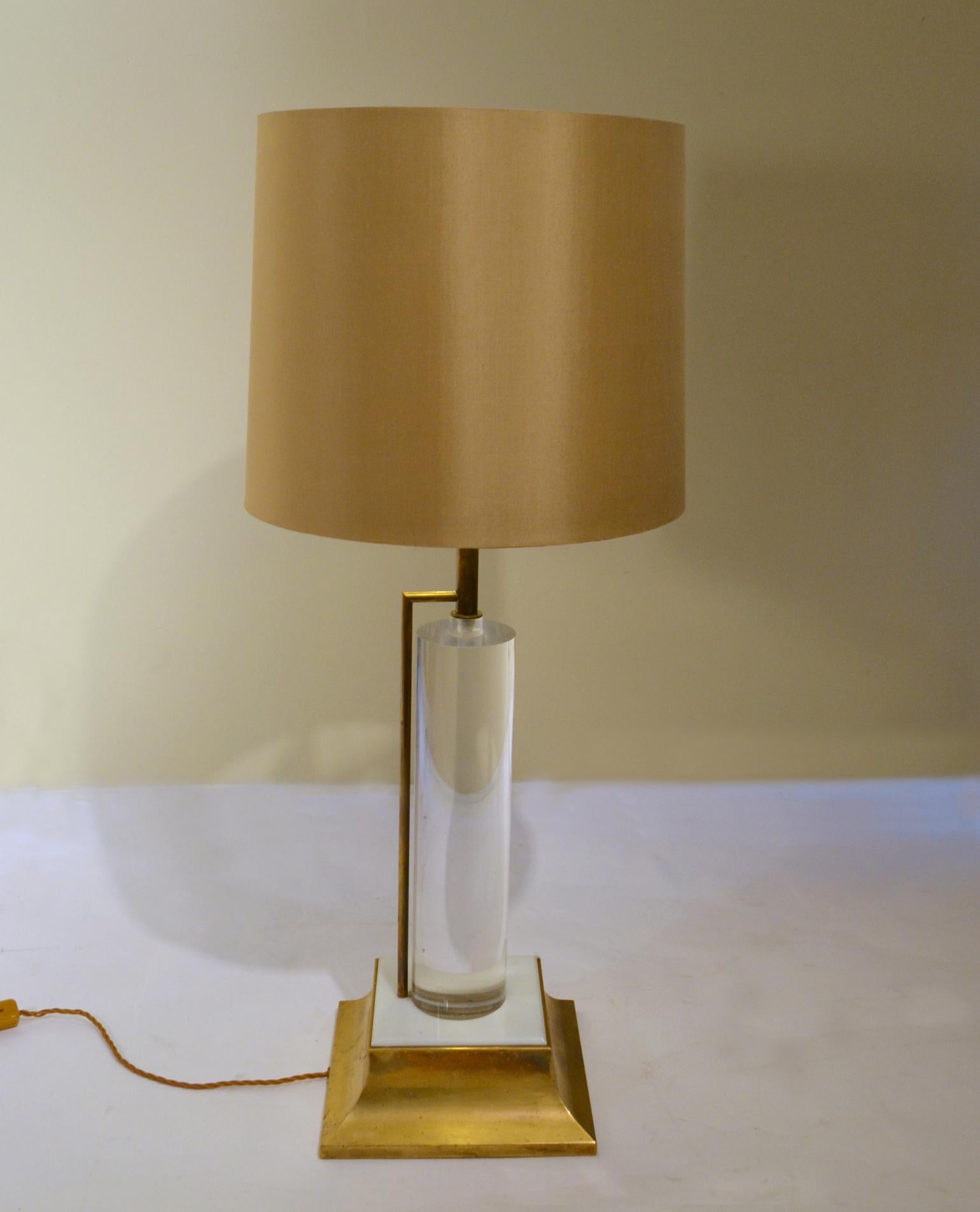 Mid Century Hollywood Regency style table lamp has a Lucite cylinder stem supported with a brass tume and base with a cream acrylic detail. Clever design, the brass supporting tube holds the wire so that the Lucite is crystal clear without visible