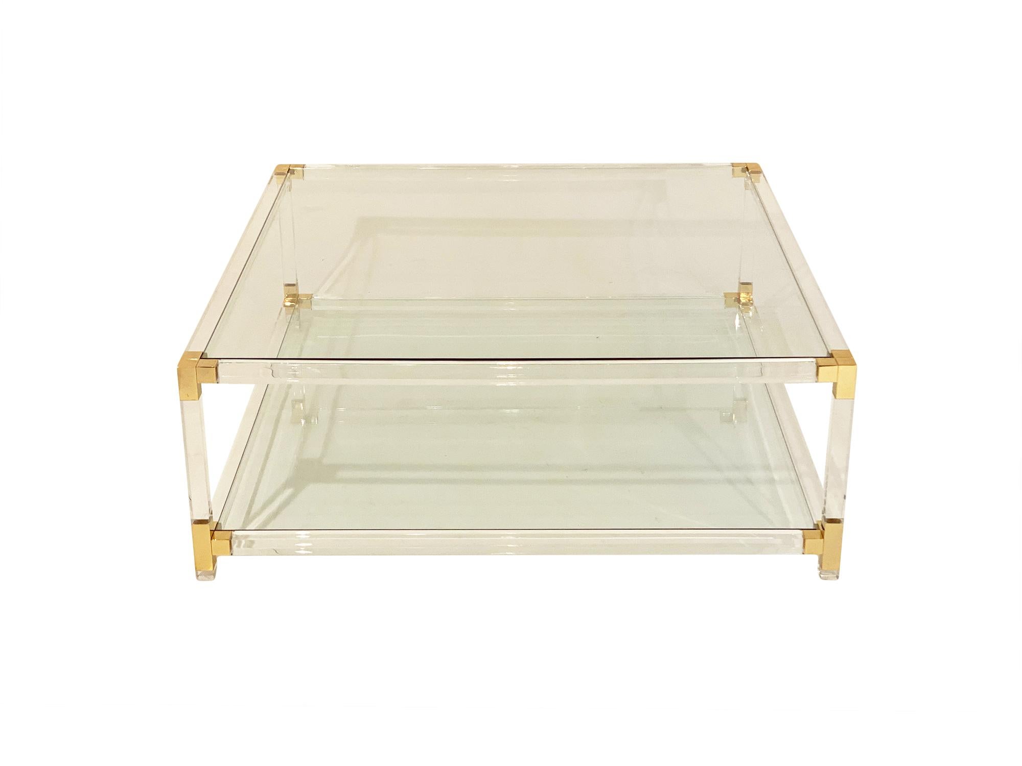 Lucite and brass large square coffee table from France. This important Modernist table has two shelves of clear glass; a strong Lucite structure, and gilt brass corner pieces. We love the impressive size and shape of this piece!