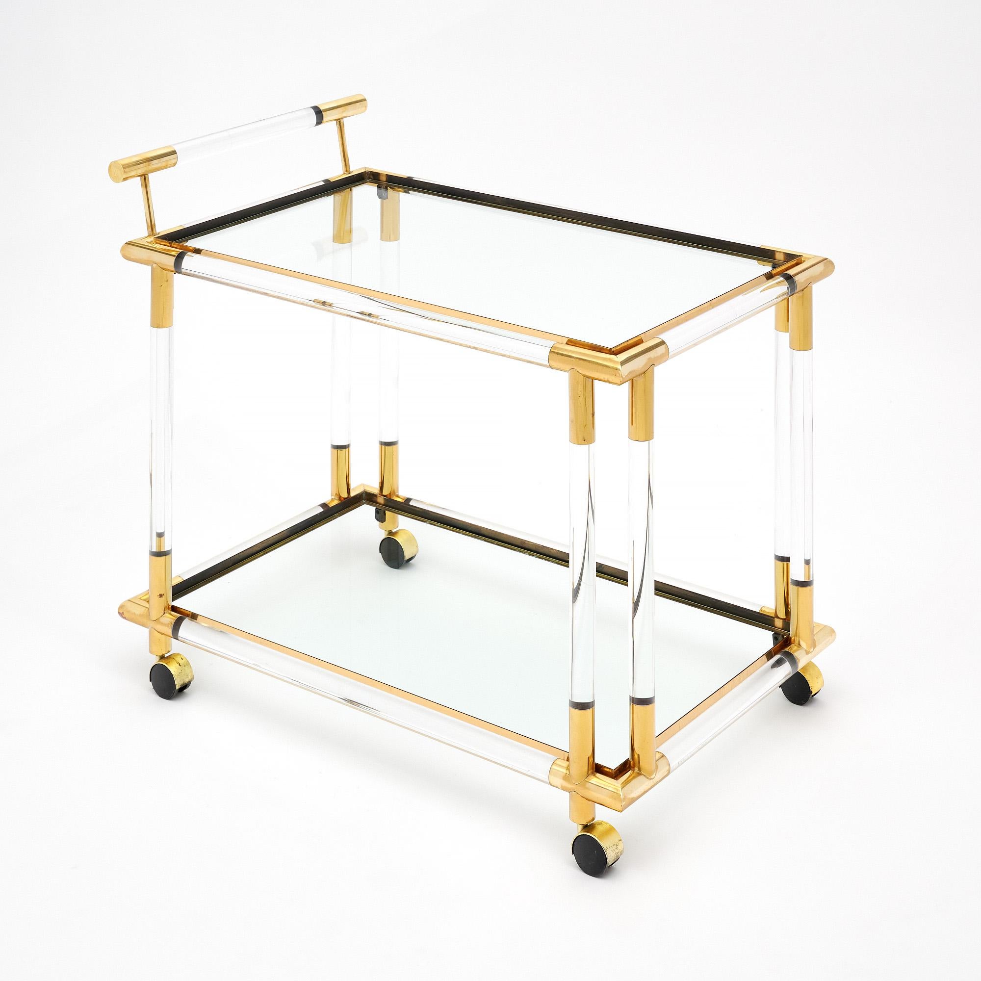 Bar cart from Modernist era France made with a Lucite structure held in place with brass. This piece has a handle and four original caster wheels. There are two shelves of clear glass. This piece is in very nice vintage condition with only minor