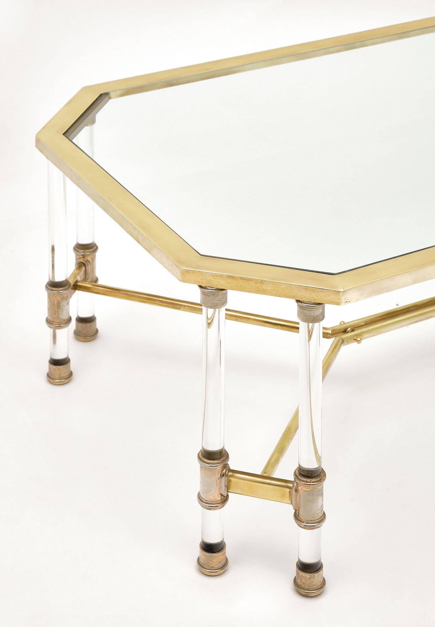 Coffee table, French, of Lucite and brass featuring a gilt brass structure with double Lucite columns in each corner. There is a brass stretcher and glass top.