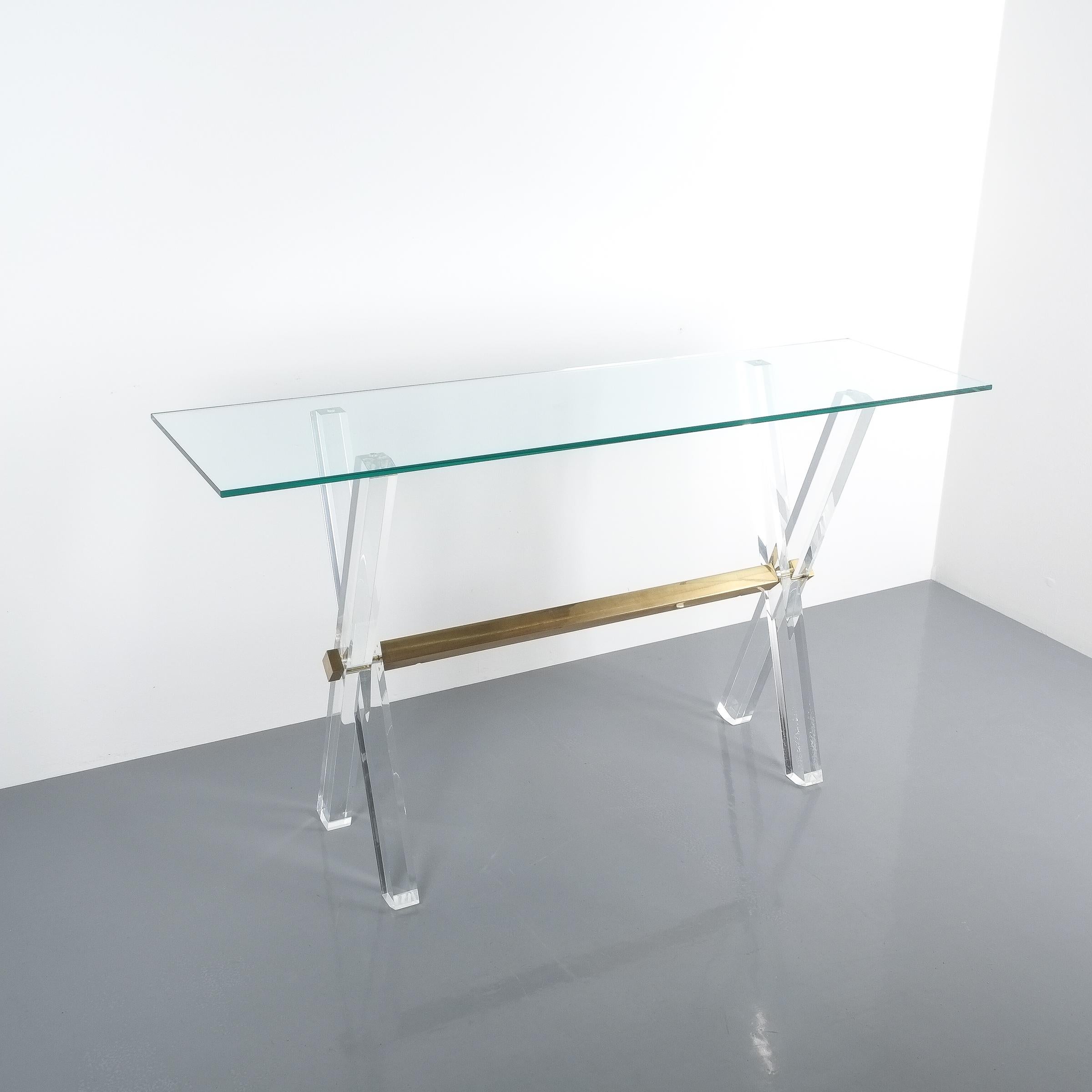 Lucite and brass X frame console table, circa 1970. Elegant console table consisting of a Lucite X frame with a horizontal polished brass beam. The glass top shows normal signs of wear with no chips present. The table is in good to excellent