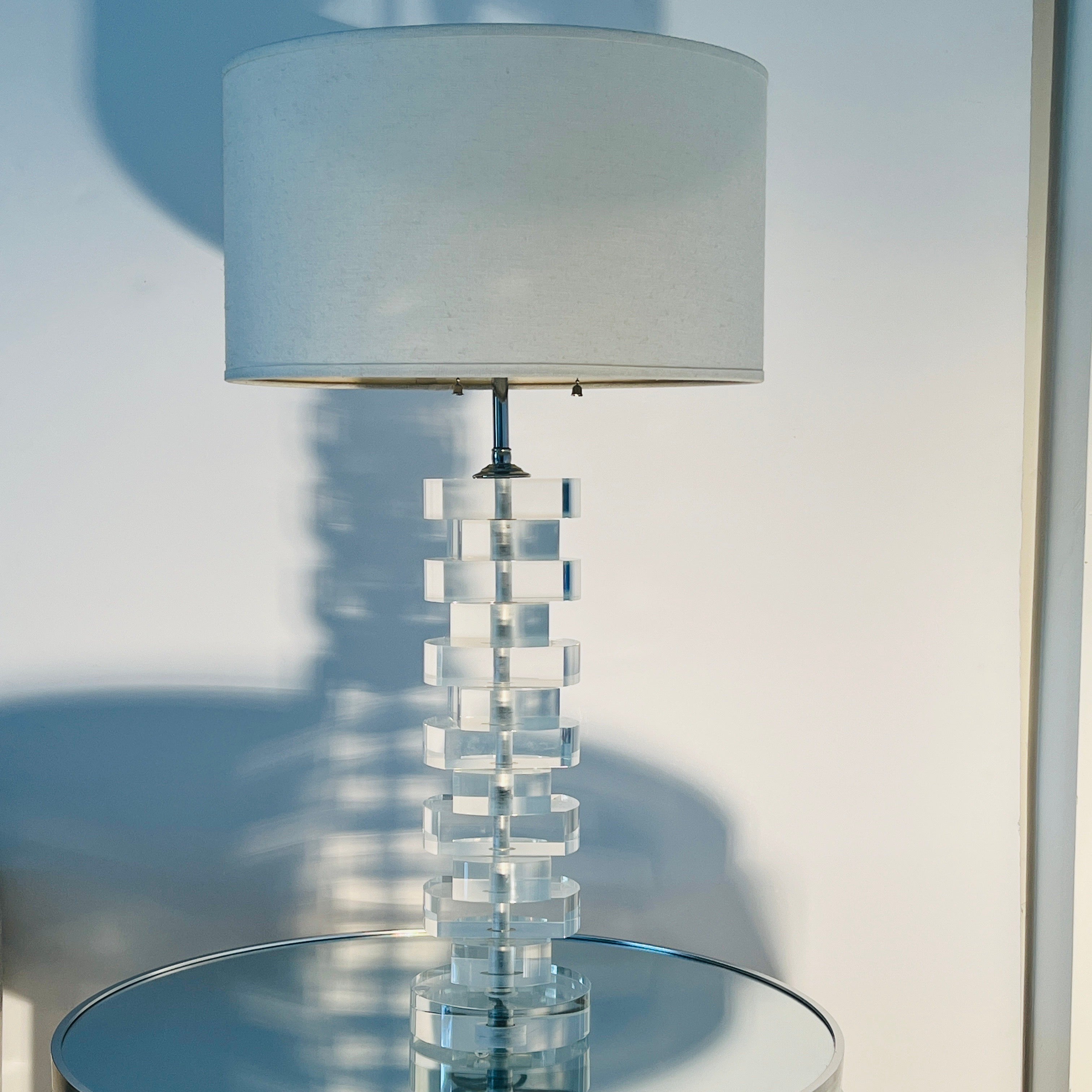 Mid-Century Modern lucite lamp comprised of stacked and beveled blocks of solid lucite.  Fitted with chrome metal stem with two lights and two pull chains. Includes linen drum shade in off-white.