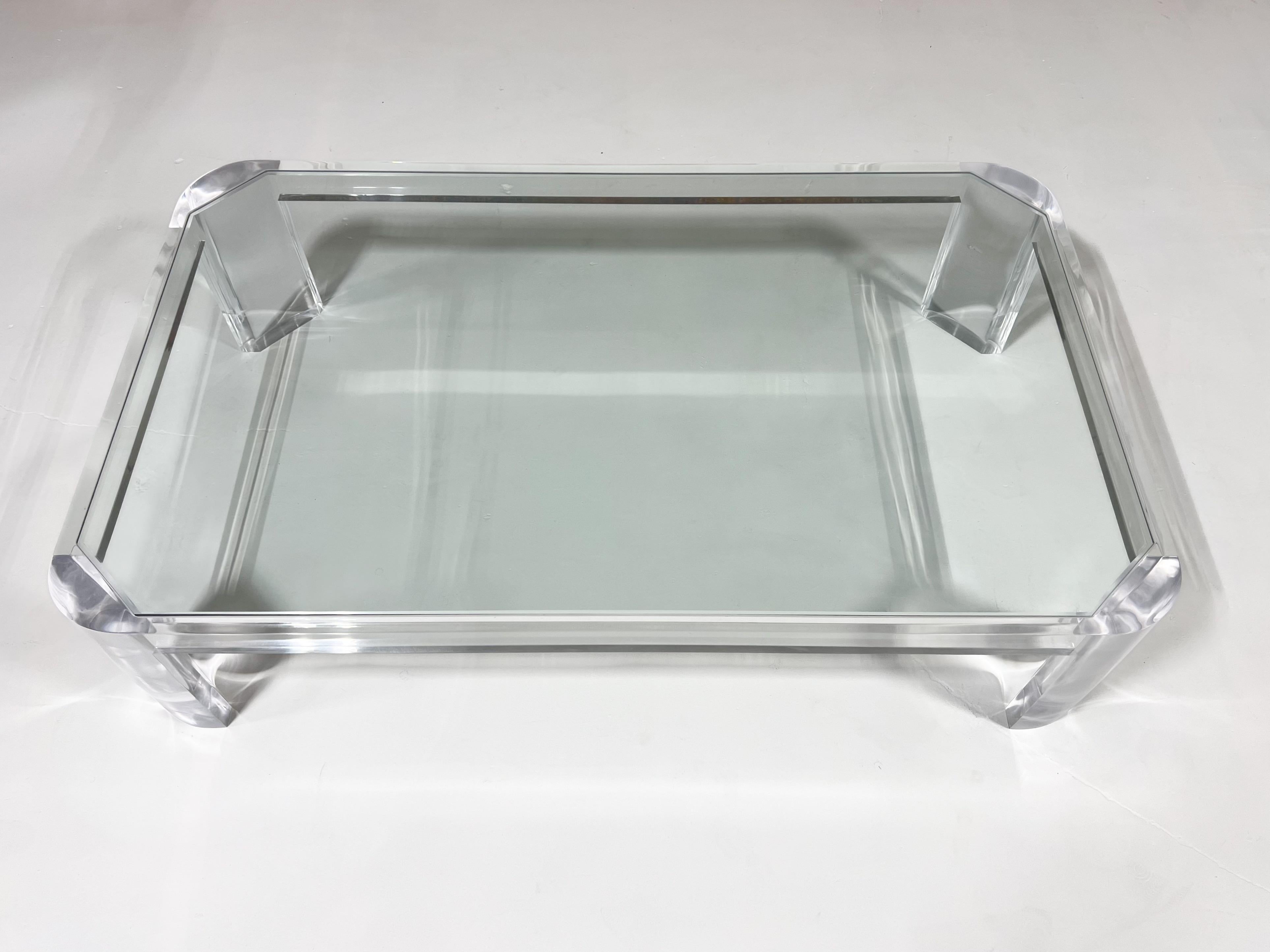 Clear Lucite with glass top cocktail table by Les Prismatiques from the 1980’s.
The glass is inserted into the frame. 
In beautiful vintage condition with minor wear consistent with age. 

Measurements: 66” Wide, 50” Deep, 16” High. 