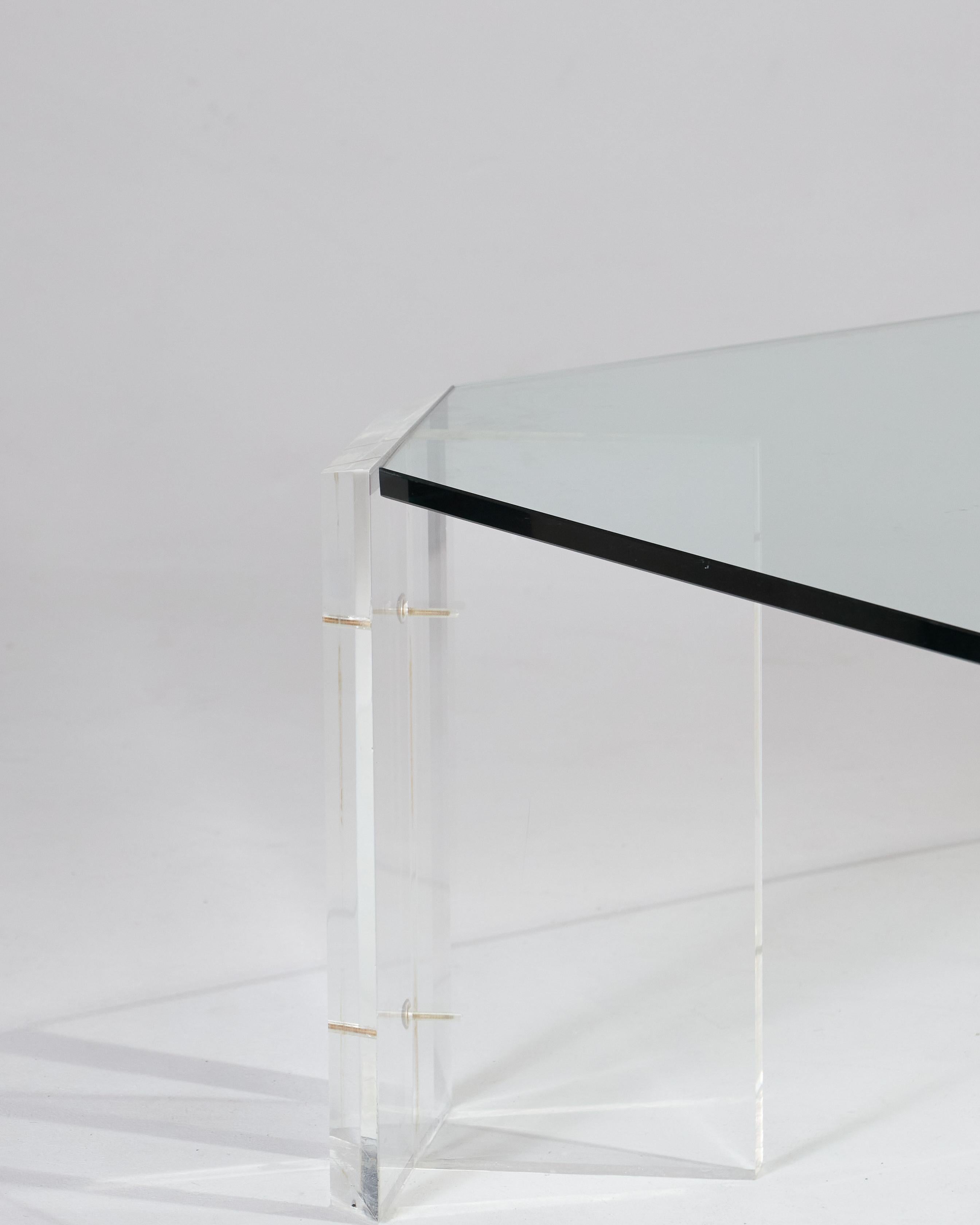 Mid-century modern octagonal coffee table attributed to designer Karl Springer, dating from the 1970s. It features four prismatic Lucite legs supporting a thick glass top. The combination of clean lines and transparent materials gives the piece a