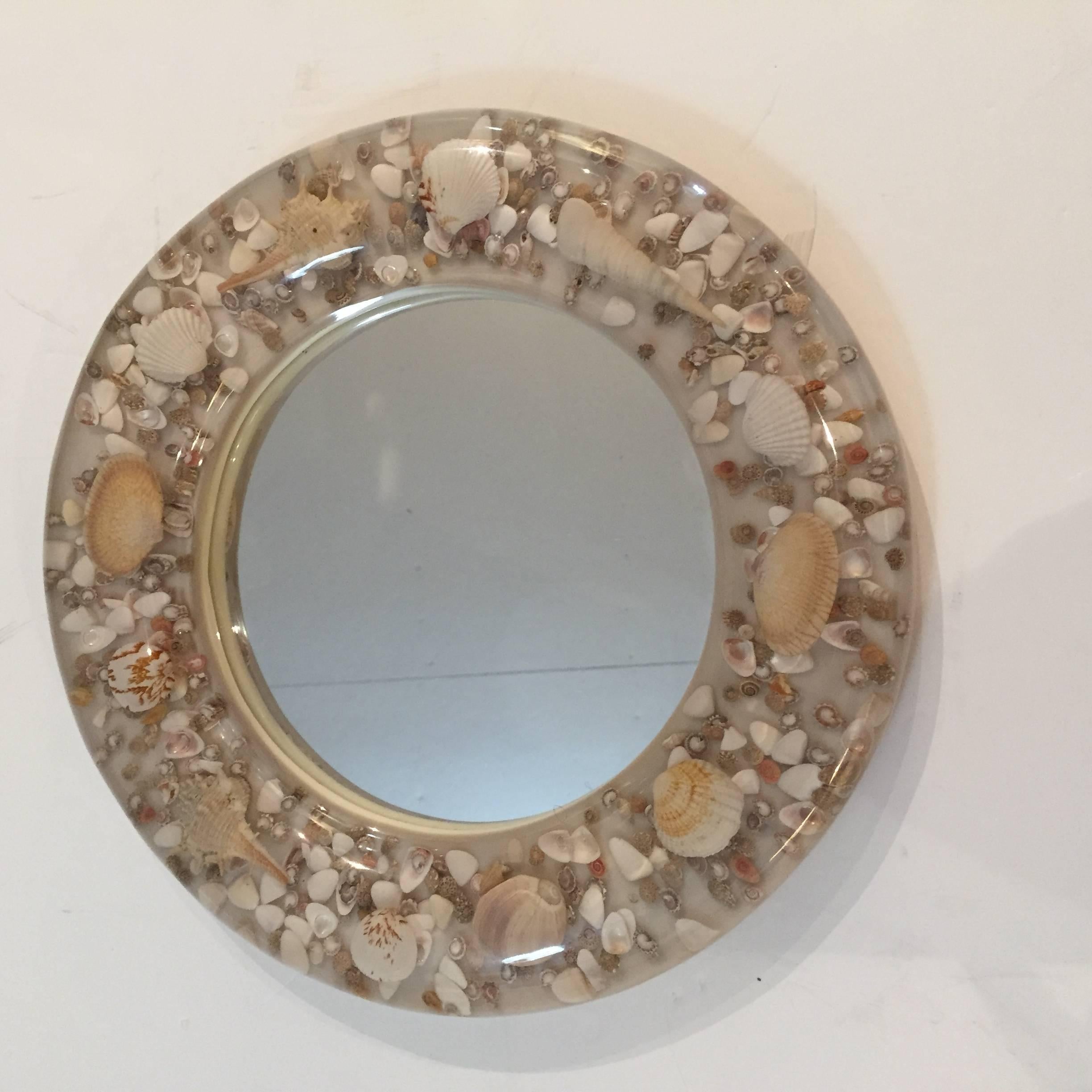 Lovely small round decorative mirror having a clear acrylic Lucite frame filled with a collection of seashells that appear to float in space.