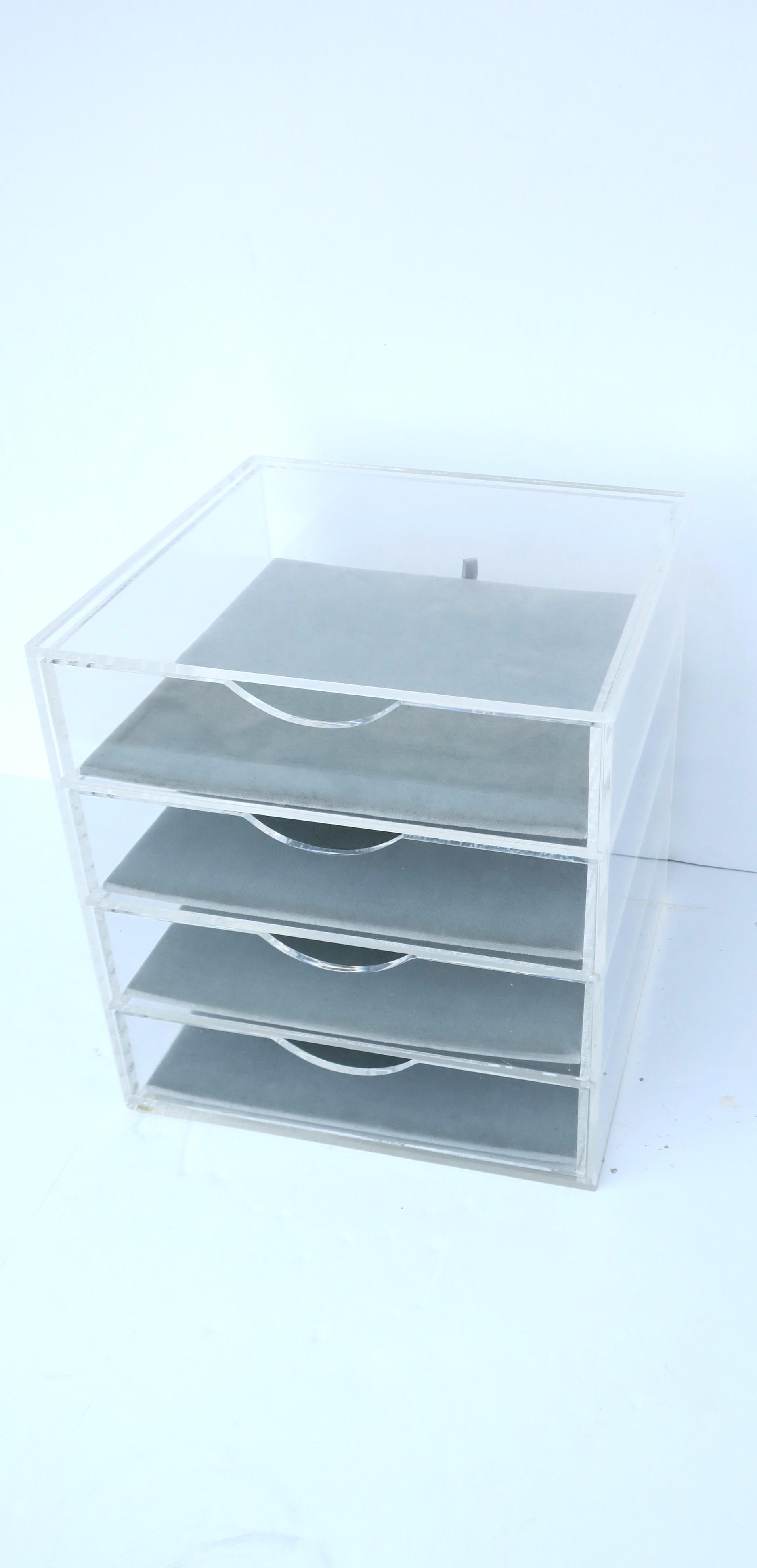 A Lucite and velvet jewelry box with storage draws, in the Modern style, circa late-20th century. Box has ample room with four (4) storage draws lined with removable velvet cushions. Cushions are a light blue/grey blue hue. Draws have an easy