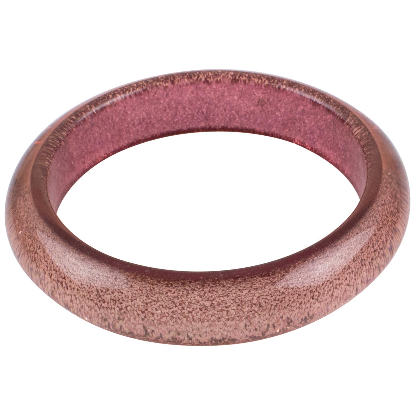 Striking Lucite bracelet bangle. The bangle has a domed shape and is comprised of transparent Lucite, which has metallic confetti injected inclusions in pink color. The metallic confetti has a texture, and glitter is like the lame fabric. There is