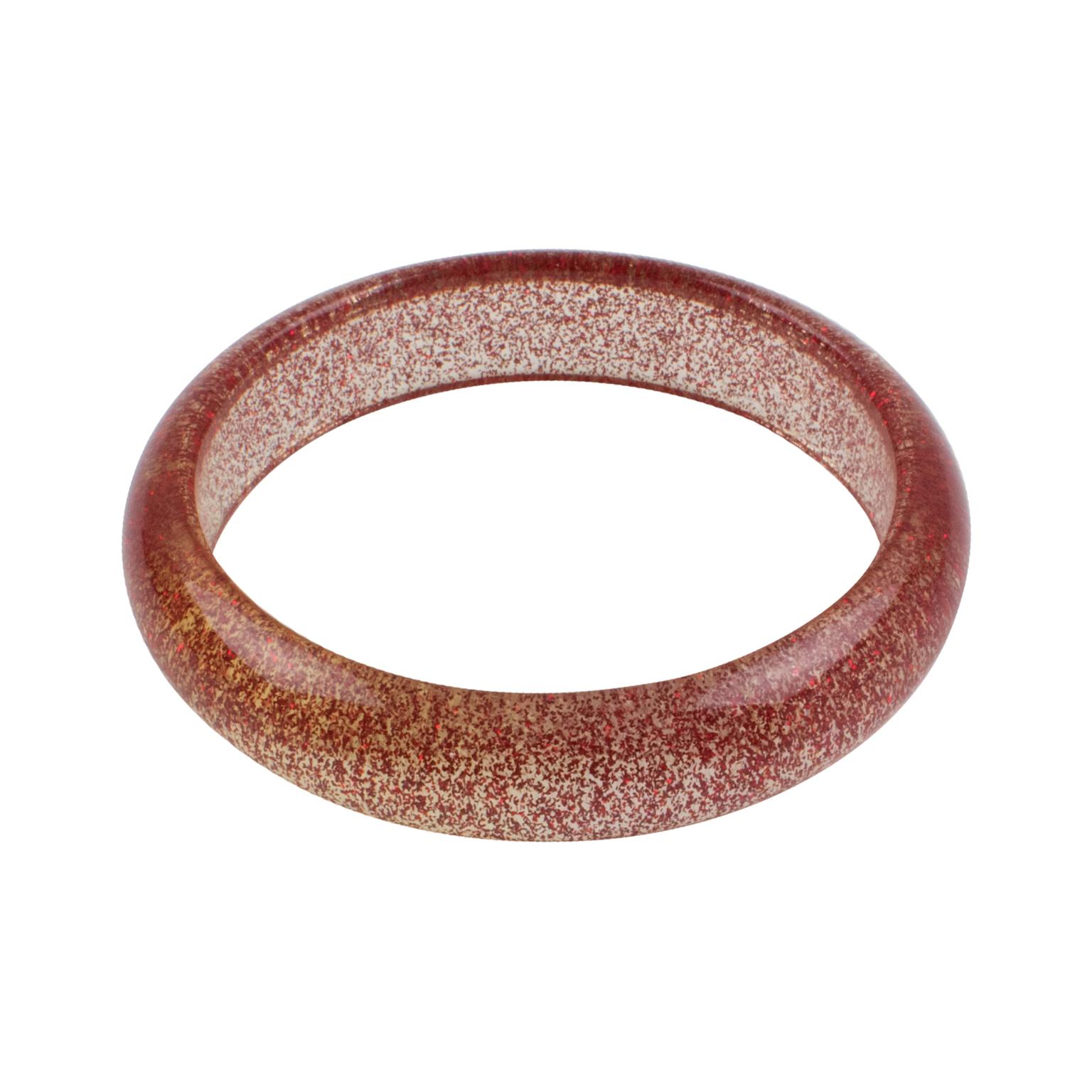 This charming Lucite bracelet features a  domed bangle shape in clear Lucite injected with metallic confetti inclusions in red color. The metallic confetti glitter is like that of Christmas decorations. There is no visible maker's