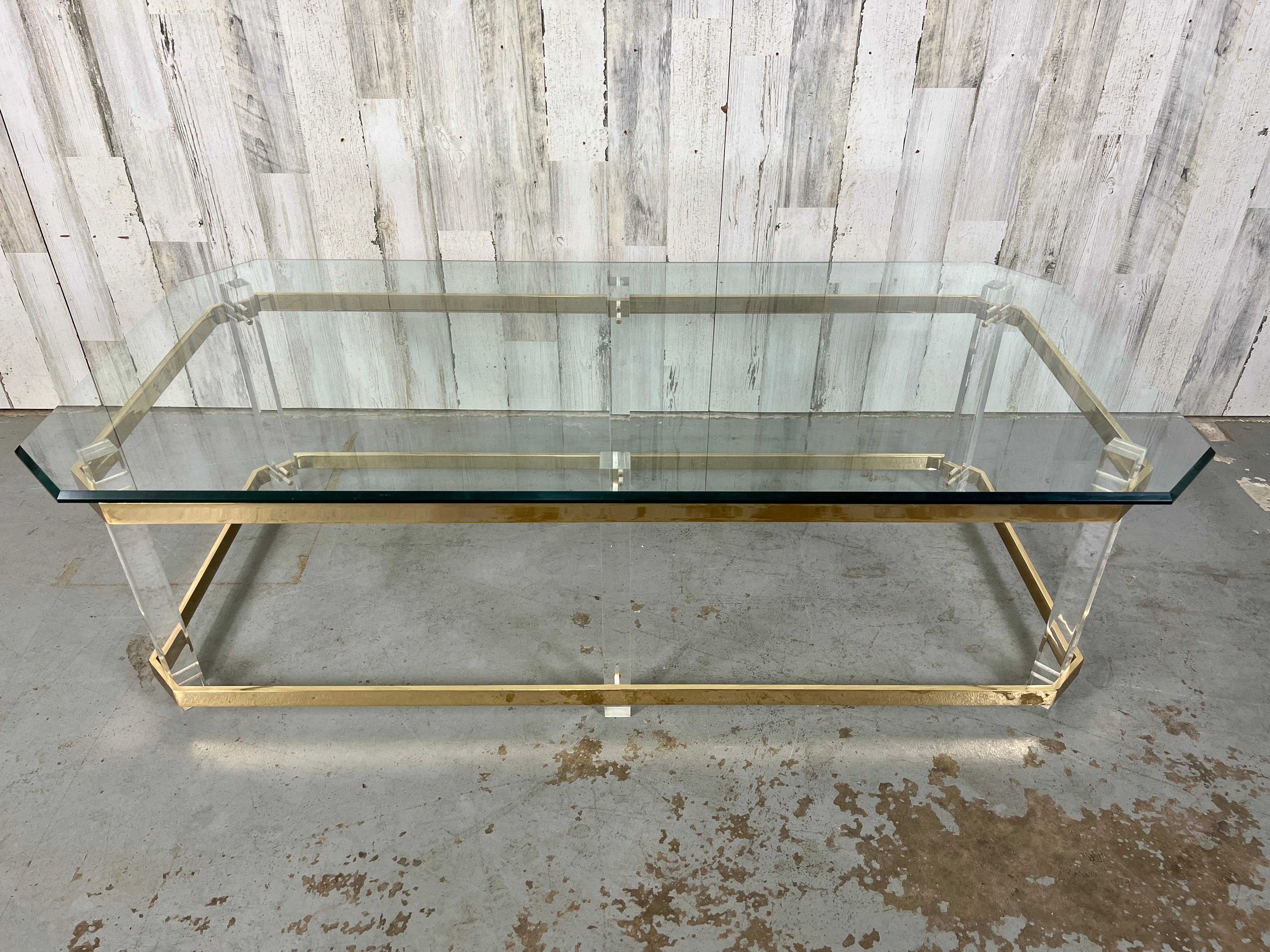 Golden glow of the polished brass stretcher and top rim offset the six lucite legs with a floating beveled glass top with chamfered corners. This table really makes a statement Commonly referred to In the style of Charles Hollis Jones.