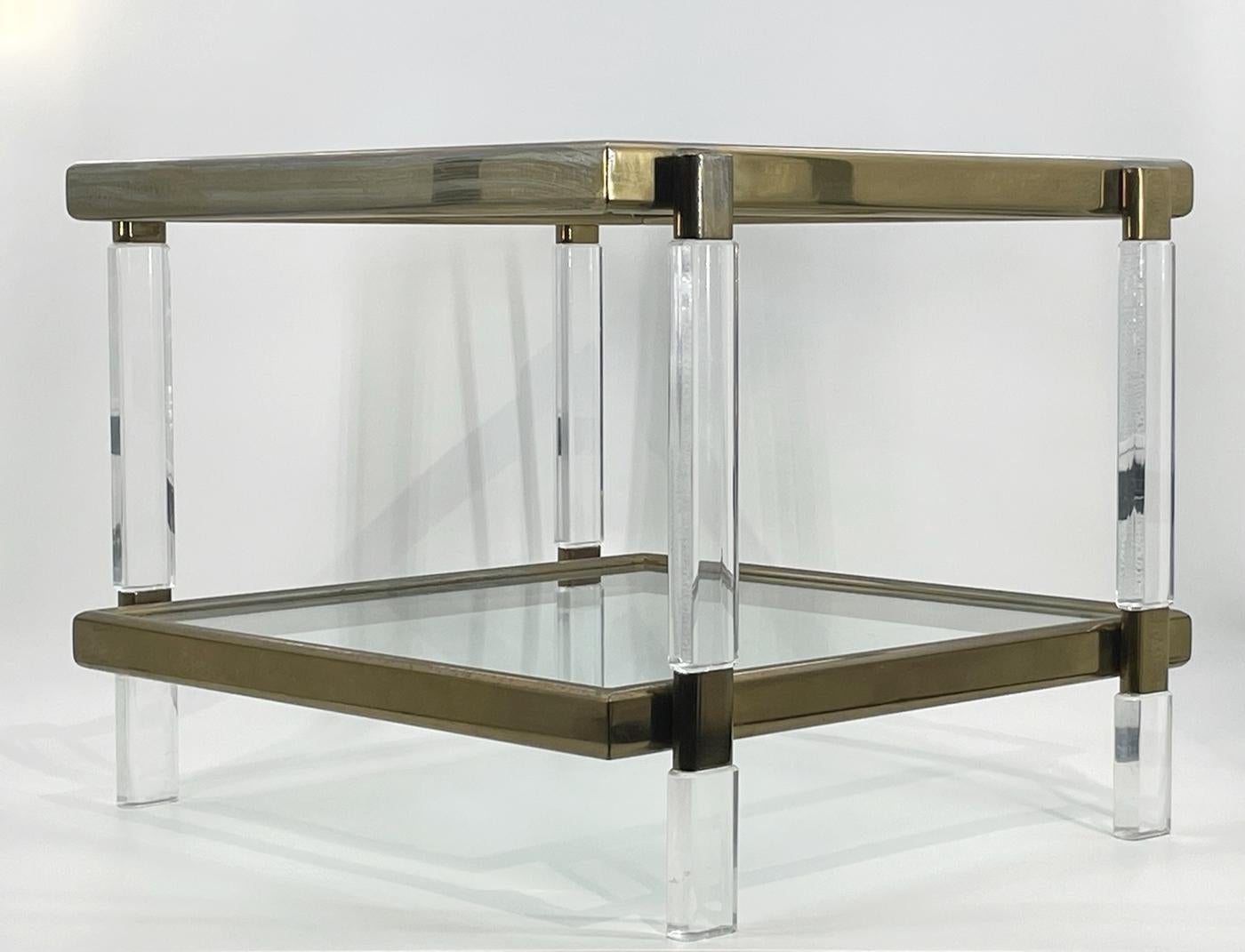 Our Lucite, Brass & Glass 2 Tier Table by Charles Hollis Jones, a stunning addition to any home or office space. This exquisite piece of furniture features a sleek and modern design with a square shape and two shelves, providing ample space for