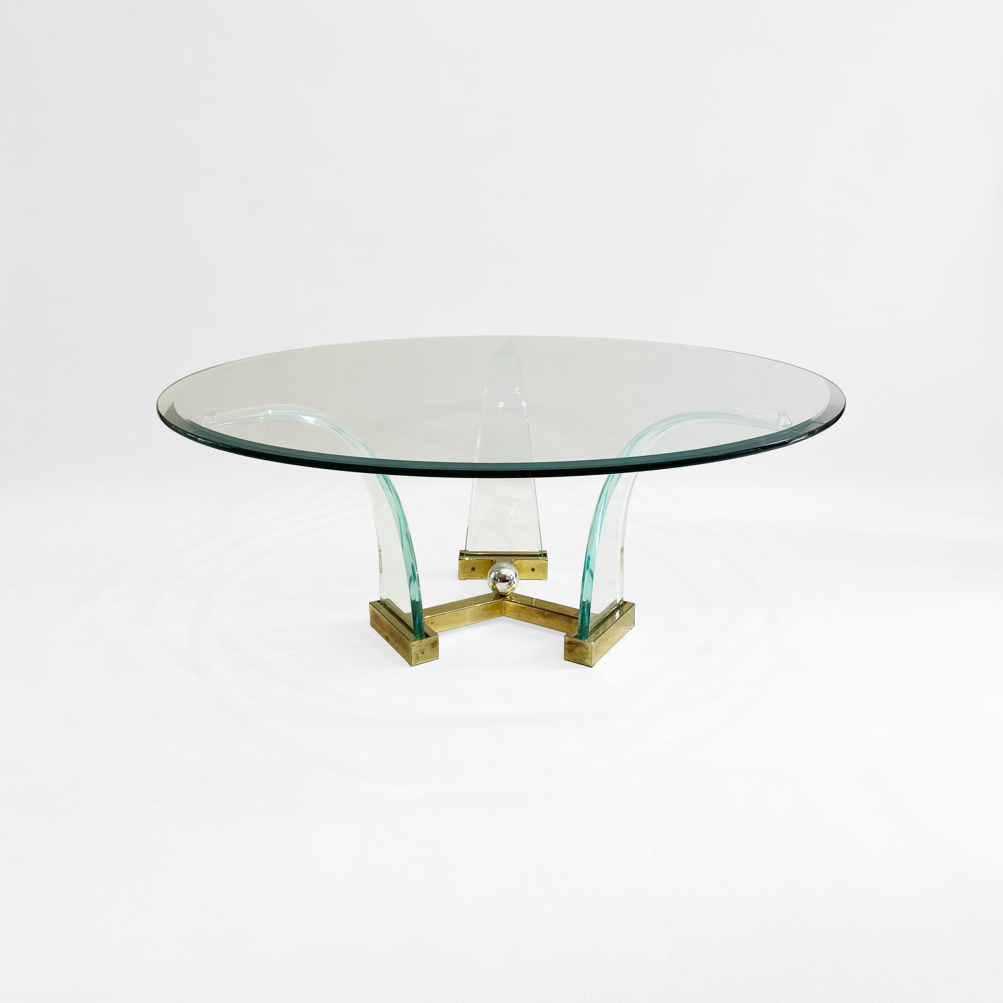 Round coffee table with lucite base in the manner of Charles Hollis Jones. The brass base supports three lucite leaf like pieces that on their return they support the round bevelled glass top.

The round shape of the coffee table is both practical