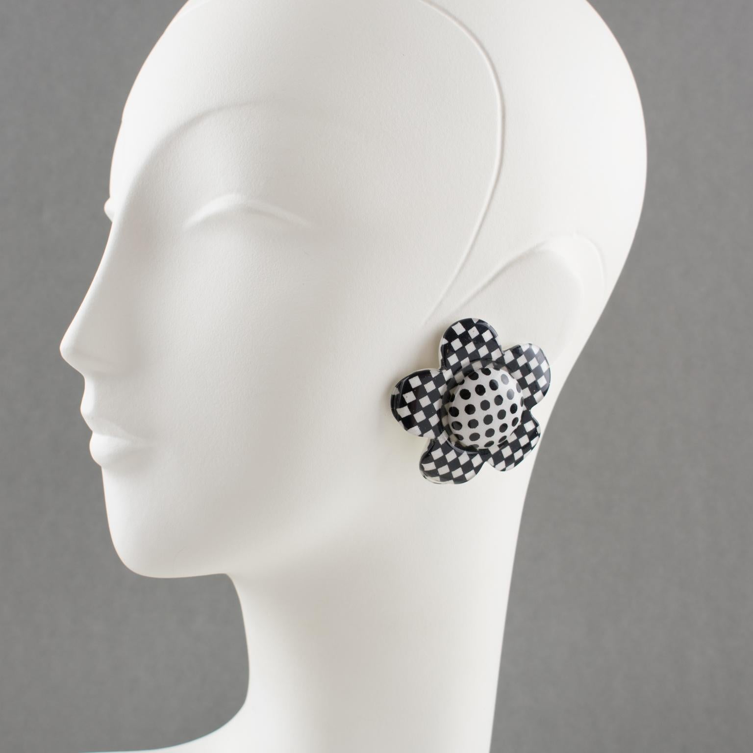These charming clip-on earrings are a vintage treasure from the 1960s. They showcase a stunning Lucite design featuring a sizeable and intricate daisy-shaped pattern. The black and white checkerboard and polka dots add a touch of whimsy and