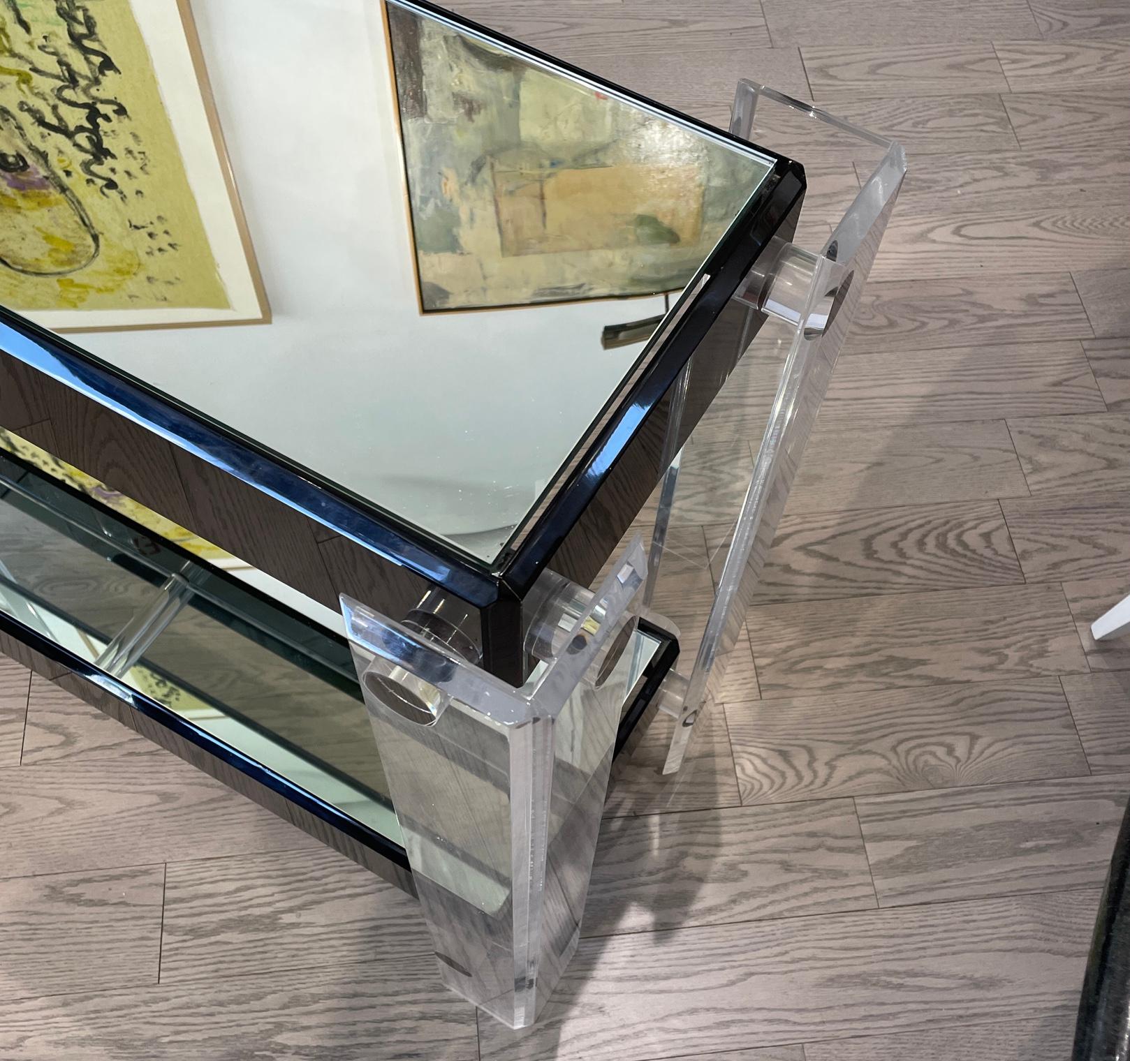 This is a nice lucite table with a mixture of clear and black lucite. It’s in the manner of Charles Hollis Jones. The top shelf is glass and the bottom shelf is mirror.