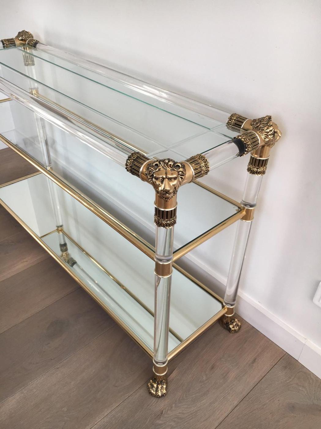 Lucite console table with gilt plastic lion heads and claw feet, French. The top shelf is made of engraved glass, the second shelf is made of clear glass and the bottom shelf is a mirror, French, circa 1970.