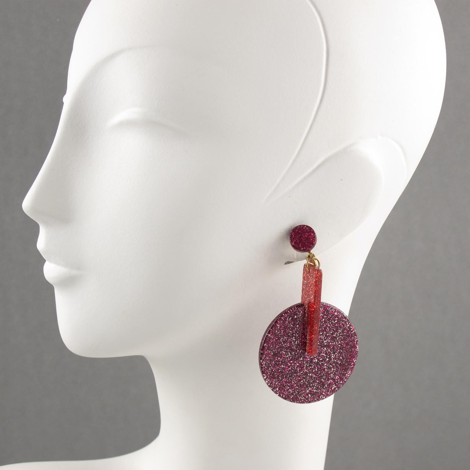 These lovely Lucite clip-on earrings feature a dangling geometric shape with glitter flakes inclusions. The pieces boast bright red and purple-pink fuchsia colors with a mesmerizing glitter effect. There is no visible maker's mark.
Measurements: