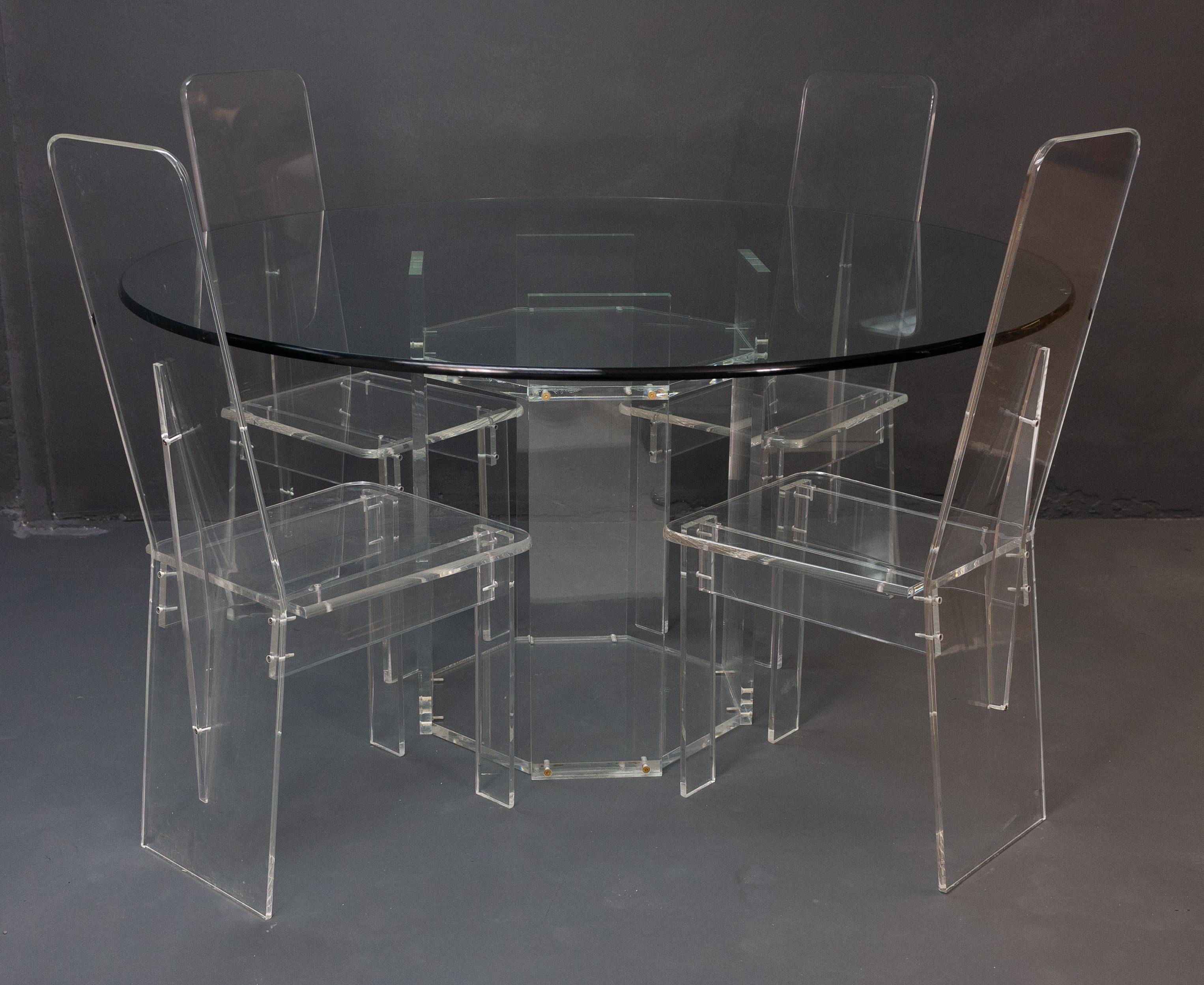 Lucite dining room set consisting of four high back dining chairs with a matching dining table. The large dining table features a thick glass top, with a beautifully rounded edge which matches the edges on the chairs. This set is made of a clear