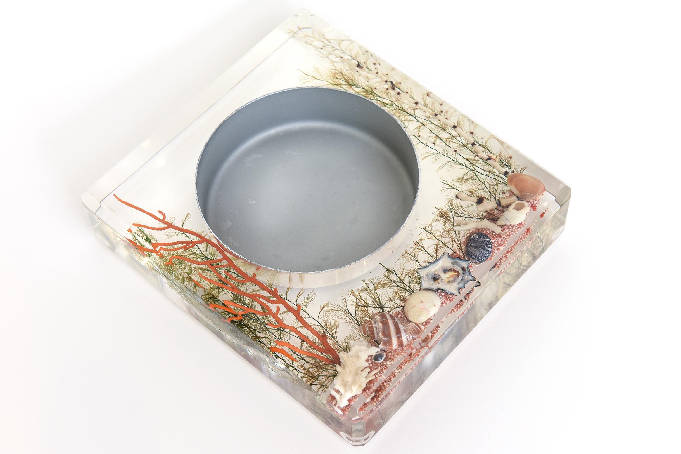 This fun, nautical and very Palm Beach lucite embedded bowl has a center of polished aluminum. The interior are assorted colored shells, resin coral, colored orange sand, and dried plants. Vintage from the 70's. Makes a great desk accessory or soap