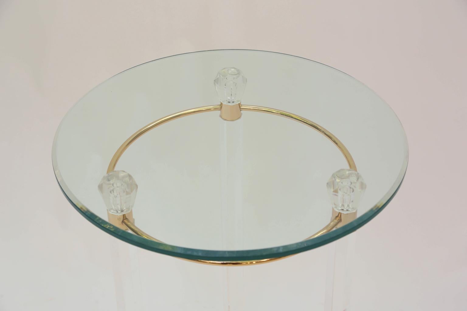 Occasional table having a round top of glass, on a classical formed base of Lucite; four columnar legs headed with faceted knobs over brass collars and central ring, joined at the feet by tripartite concave stretcher of brass. 

Stock ID: D2402.