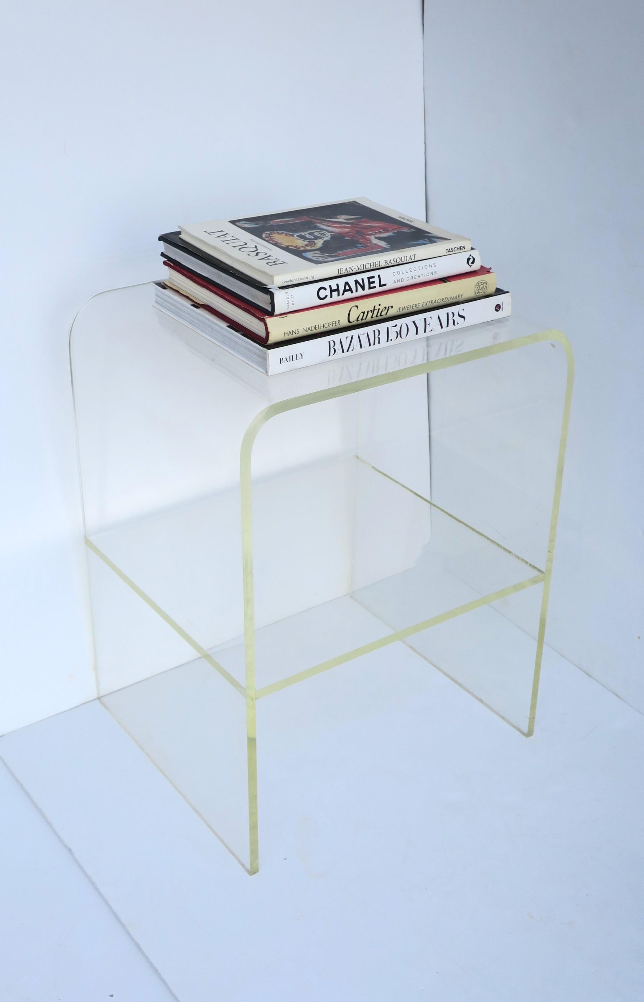 A substantial and well-made Lucite end table with storage shelf in the Modern style, circa late-20th century. Lucite table has a waterfall edge and storage shelf area. Great as an end table or as a storage piece in bath area, etc. Many uses.
