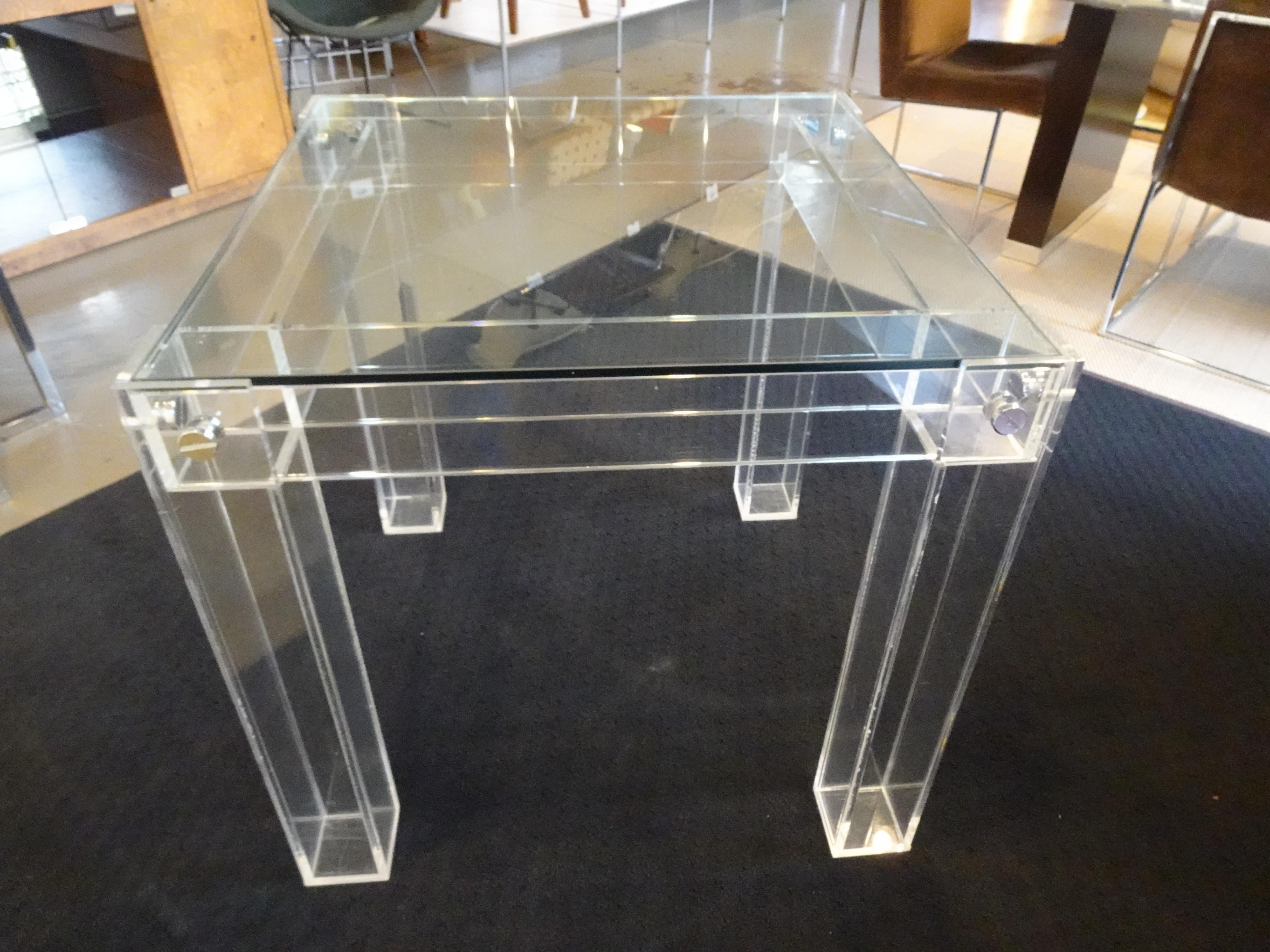 A well made Lucite Game table or small dining table with squared legs and frame structure with drop in plate glass top. Huge chrome screws attached the legs to the top frame giving the piece added detail and strength a great sized piece for a small