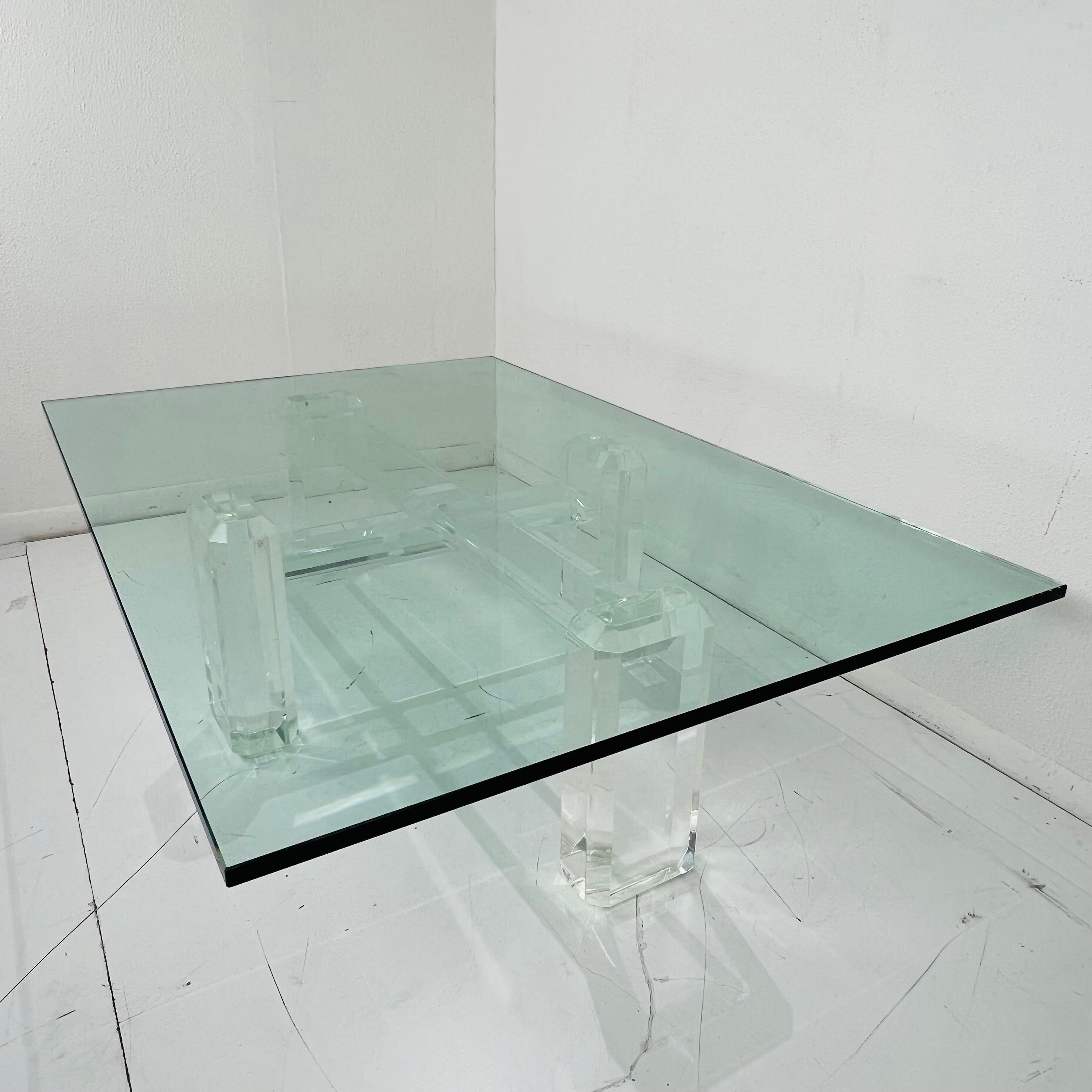 Gorgeous 1980s Monumental Lucite coffee table with glass top, attributed to Karl Springer. Bulky pillar legs meet in a cross shape to support the thick glass resting on top. Beautiful condition, lucite is clear and has minimal scratches/scuffs.