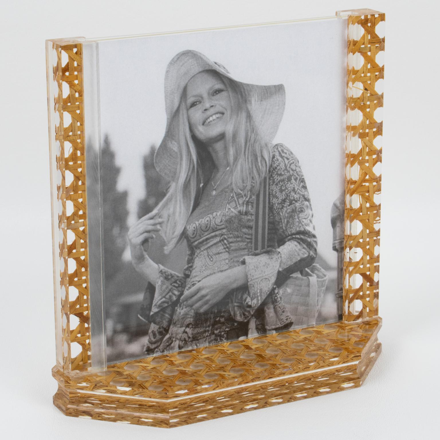 This lovely modernist picture photo frame was crafted in Italy in the 1970s. The piece boasts a hexagonal thick Lucite slab base with two tall holders. The frame is made of clear Lucite with genuine rattan, wicket, or cane work embedded in the