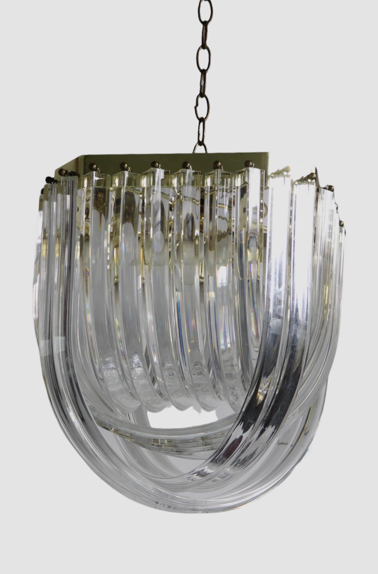 Sexy Post Modern, Art Deco Revival, Hollywood Regency lucite ribbon chandelier, in very good, original, clean and working condition. This statement chandelier features four interior sockets, creating an intriguing glow, and ample light when lit.