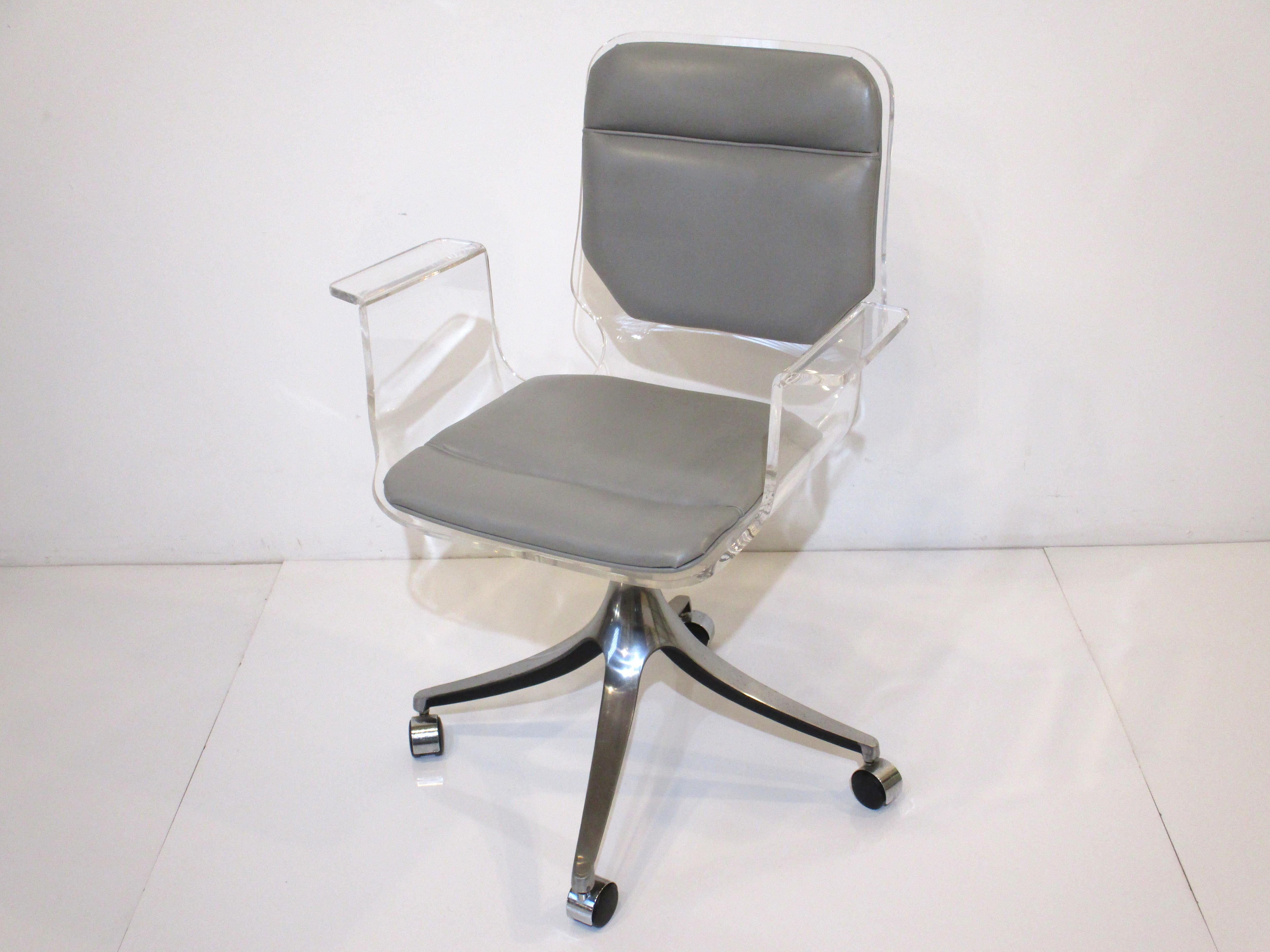 A sculptural rolling Lucite desk chair with sky blue leatherette seat back and bottom having a polished cast steel base with black wheels. A very comfortable chair with wing styled armrests perfect for that Lucite or glass desk crafted by the Hill