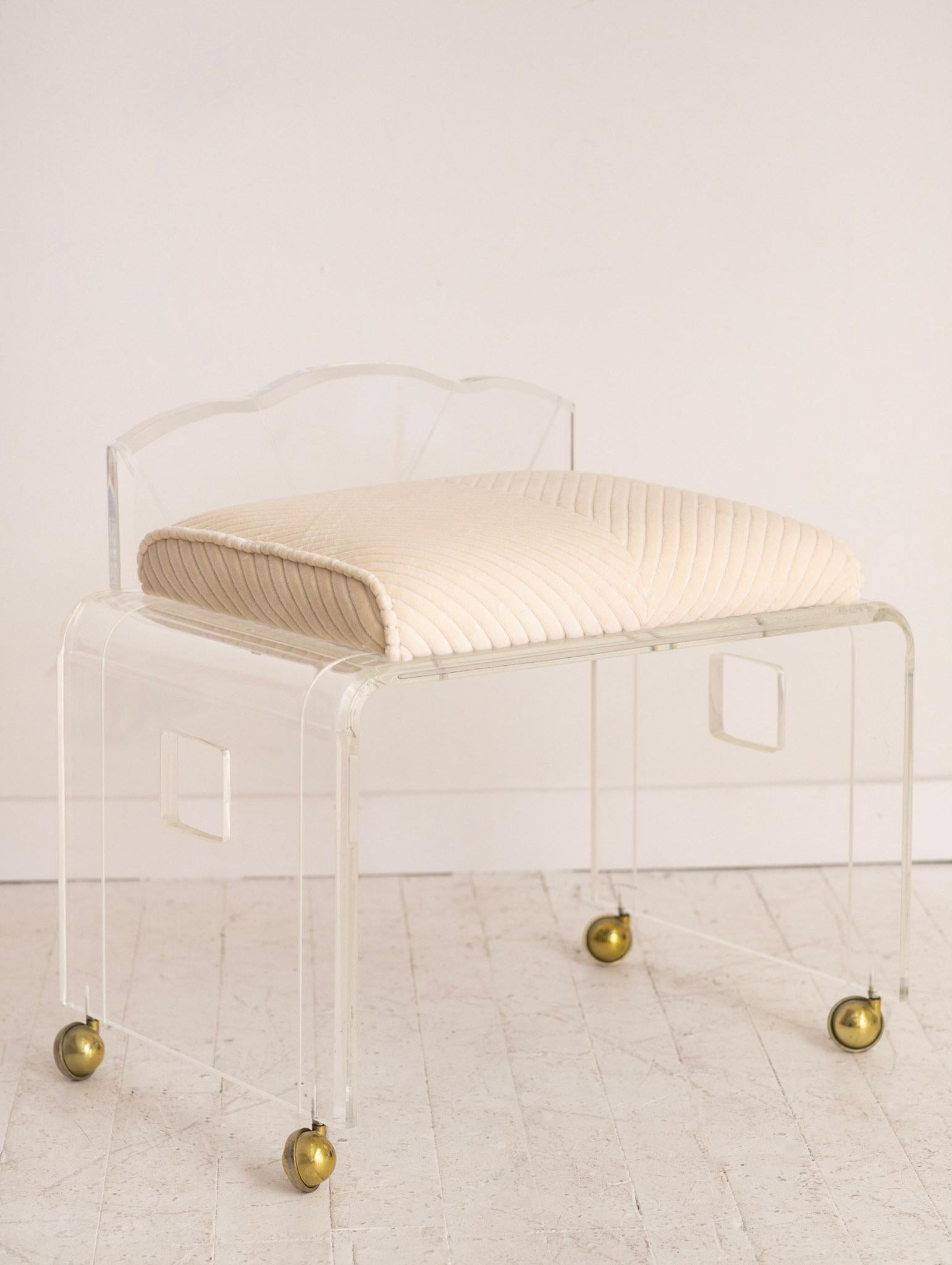 Wonderful Hollywood Regency vanity bench / stool. Heavy thick lucite. Etched back detail. Gold tone castors. Newly reupholstered. Striped cream velvet creates a herringbone pattern.
