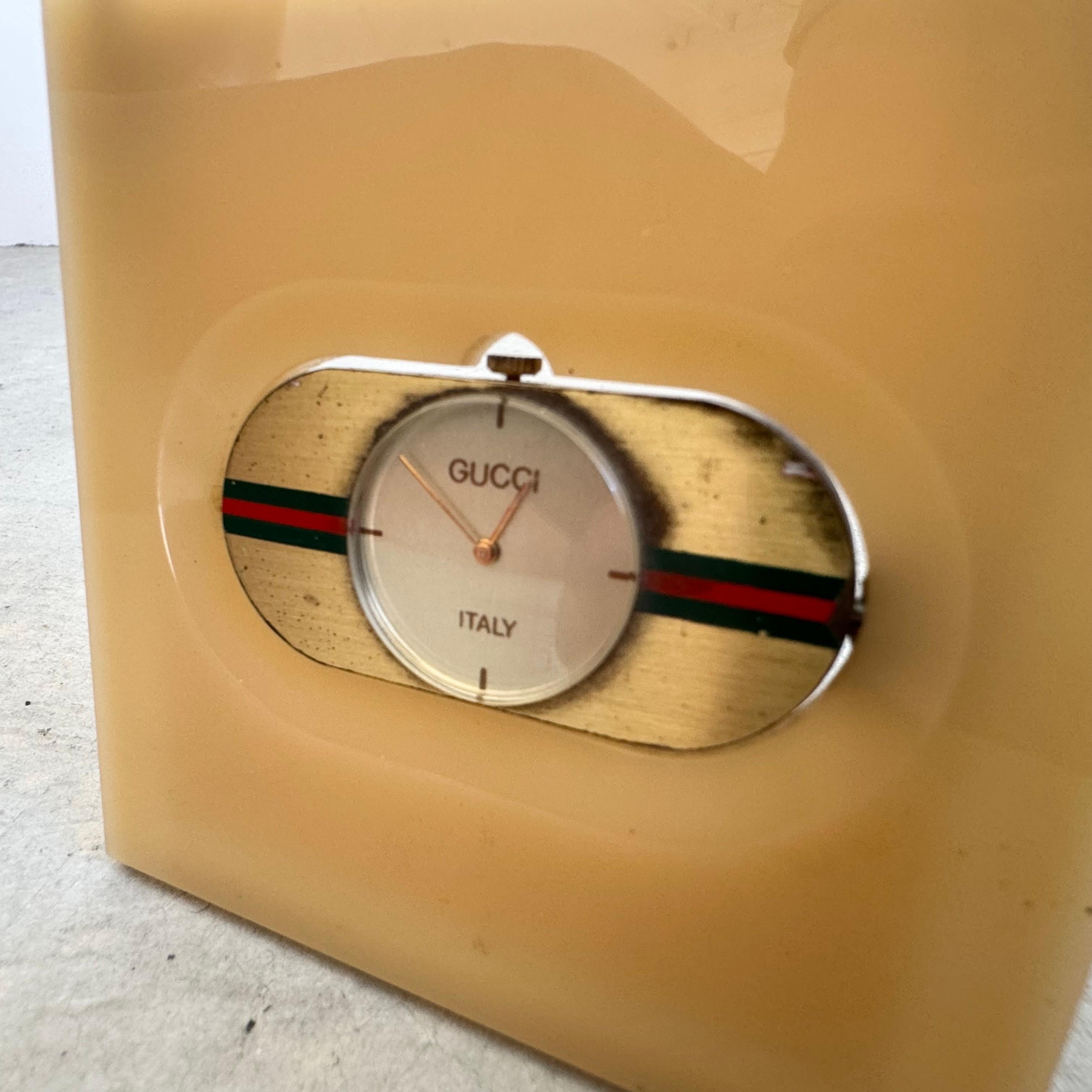 This unique travel desk clock by Gucci is a testament to quality and design. A square lucite panel encases a brass clock, which articulates vertically for ease of access to wind. A brass structure attached to the back of the panel can either lay