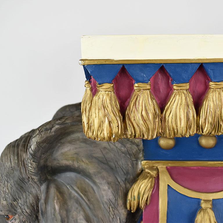 A whimsical circus elephant motif plant stand. Created from either chalkware or fiberglass, this plant stand depicts an elephant standing upon a box. His trunk is curled up (which is considered lucky in South East Asia.) He is decorated with a red,
