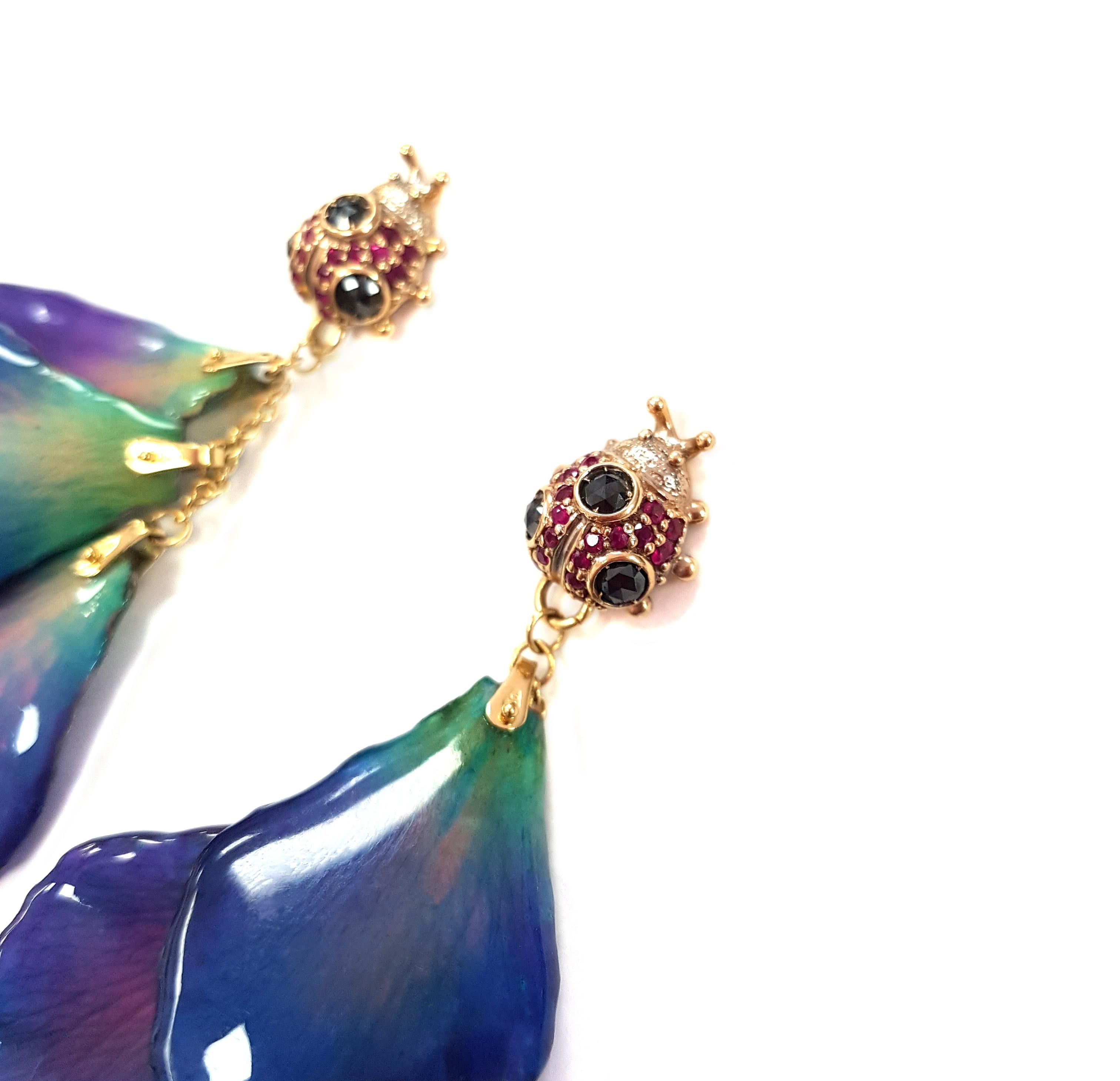 A vibrant pair of floral earrings masterfully created by hand. Each earring features three perfect petals from an actual orchid.  Each petal hangs from an 18-karat yellow gold chain which beautifully balances the cool tones of the mauve, blues and
