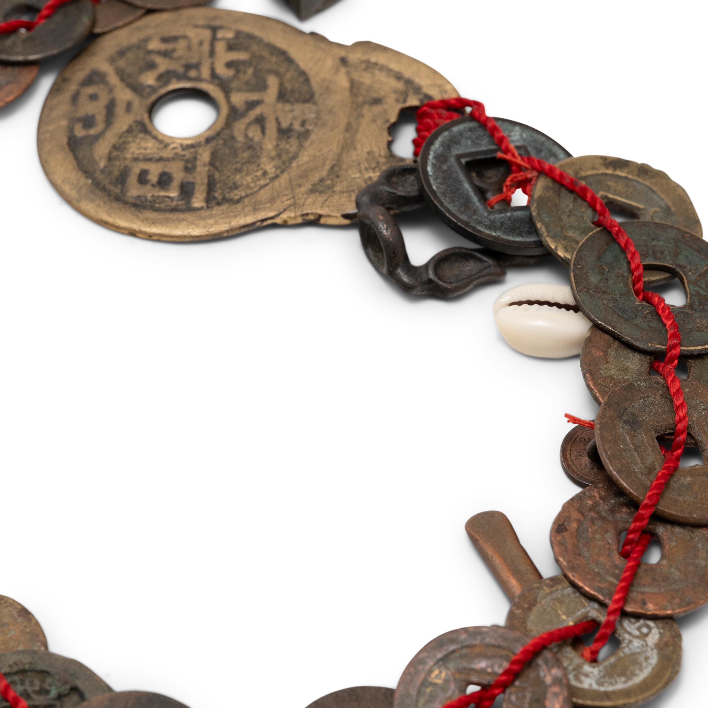 A long chain of antique Chinese copper coins and charms, strung together with red silk cord. As symbols of wealth, a string of coins is a popular talisman for beckoning prosperity and is also thought to ward off evil and misfortune. The coins are