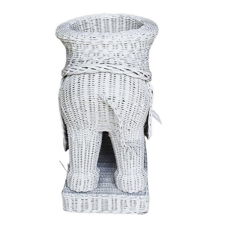A whimsical white-painted wicker elephant plant stand from the 1970s. Created from wicker, this large elephant has its trunk pointed up, a sign of luckiness in southeast Asia. It has two ears and a tusk made of wood. The top of the planter has a