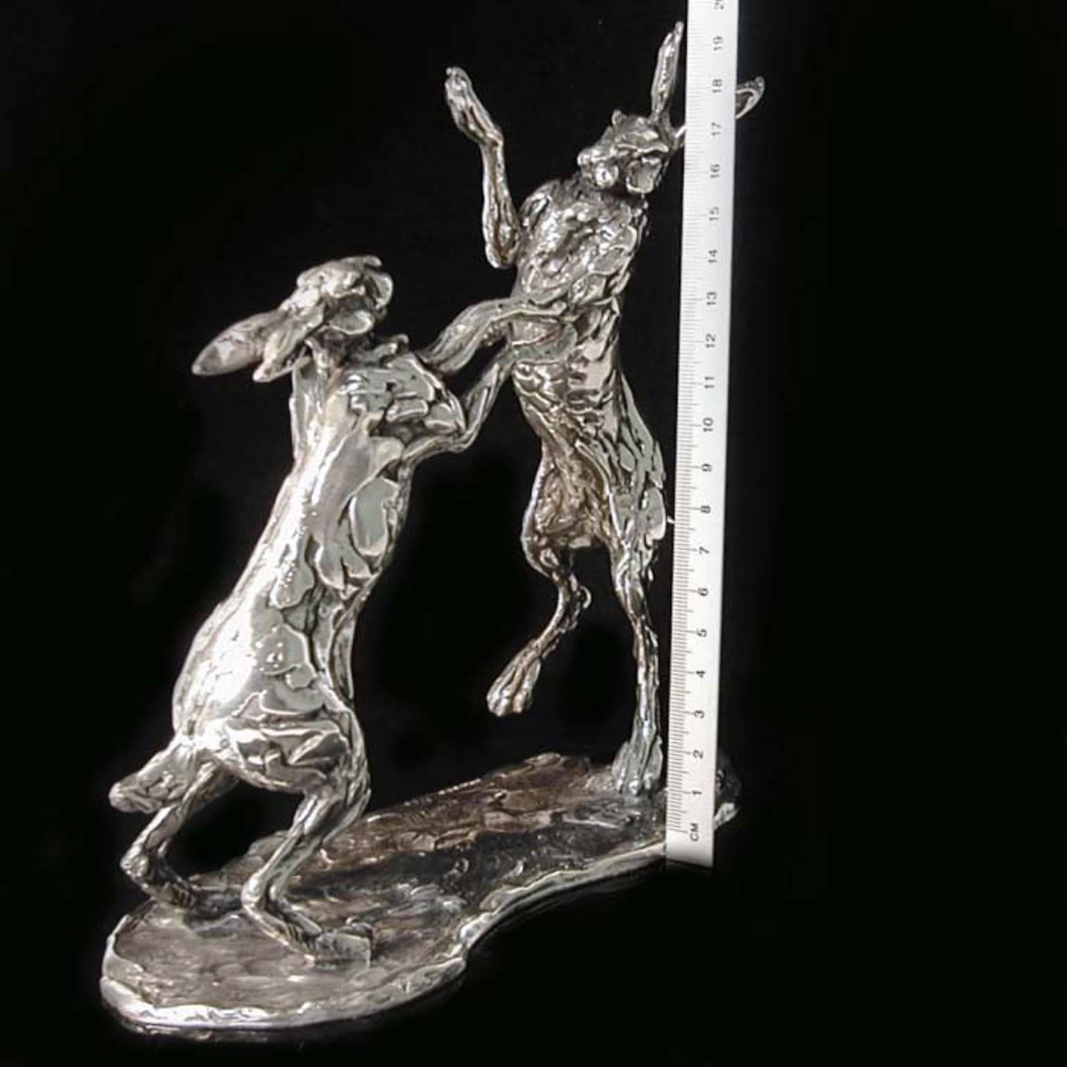 Height 20.5cm x length 20cm
1187 grams

A 'Boxing Hares' sterling silver sculpture by Lucy Kinsella, the limited edition pair of long eared brown hares caught mid boxing match, with one stood tall on stretched hind legs raining blows down on the