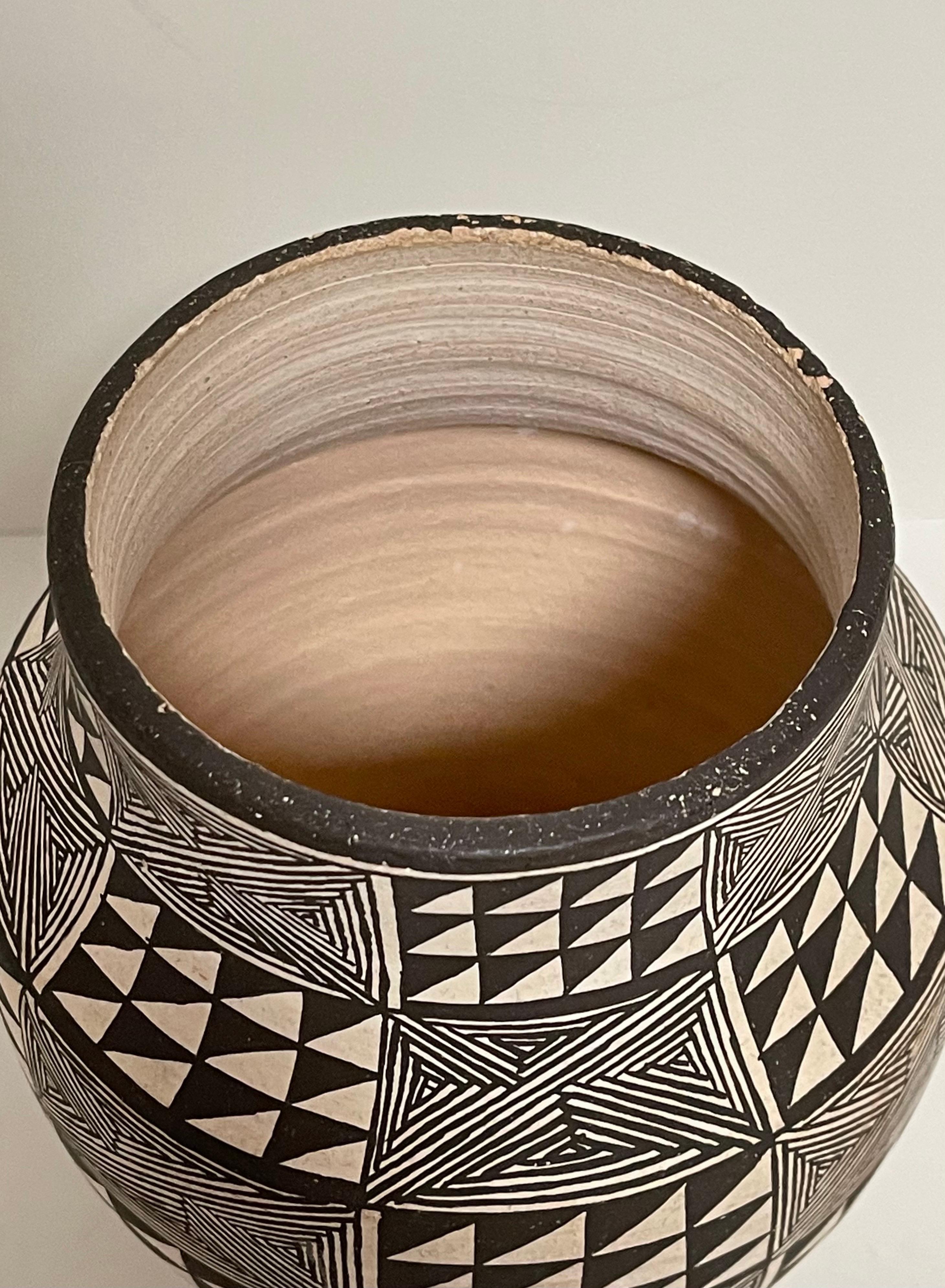 Lucy Lewis signed Acoma pottery vessel in a geometric pattern. Dated 1984. In good condition with some roughness and nicks along the top rim. Measures: 7 inches tall and approximately 6 inches in diameter.