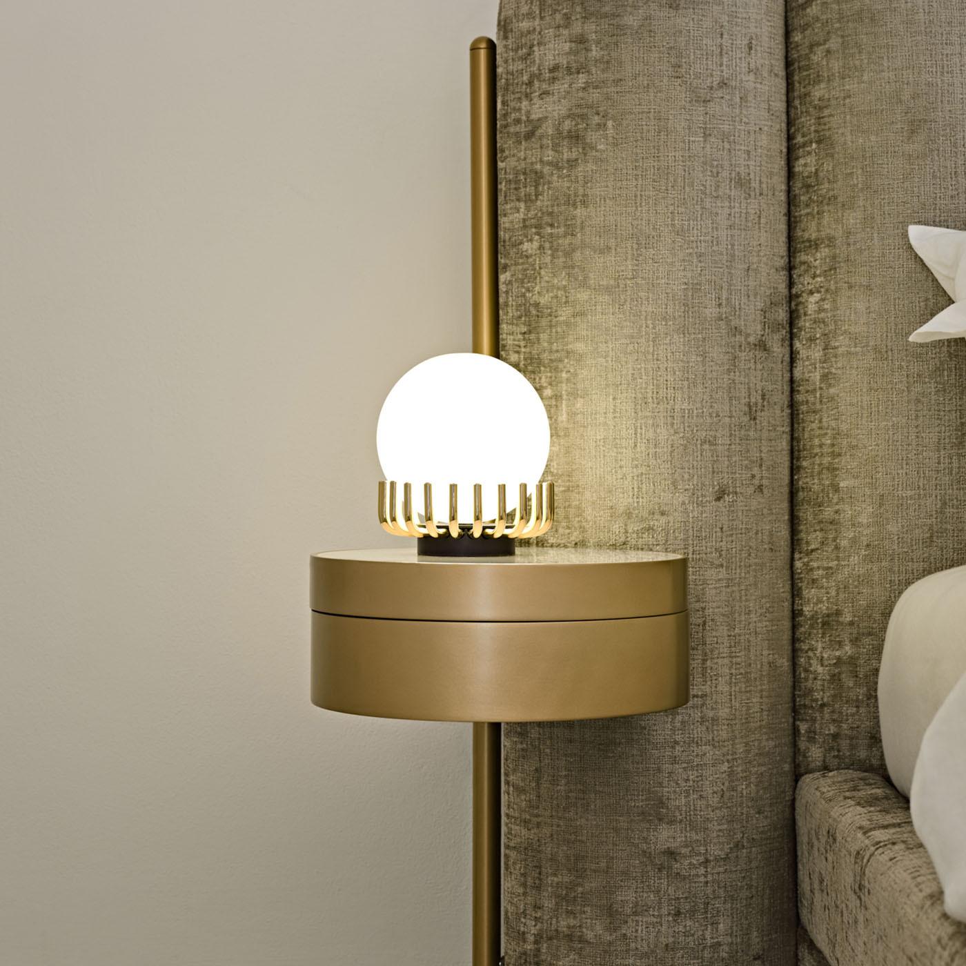 A glossy opaline glass sphere seemingly embraced by rays surrounding its base is the distinguishing element of this table lamp. The curved cylindrical elements in galvanized golden metal stem from a round-cut base are finished in matte black for a